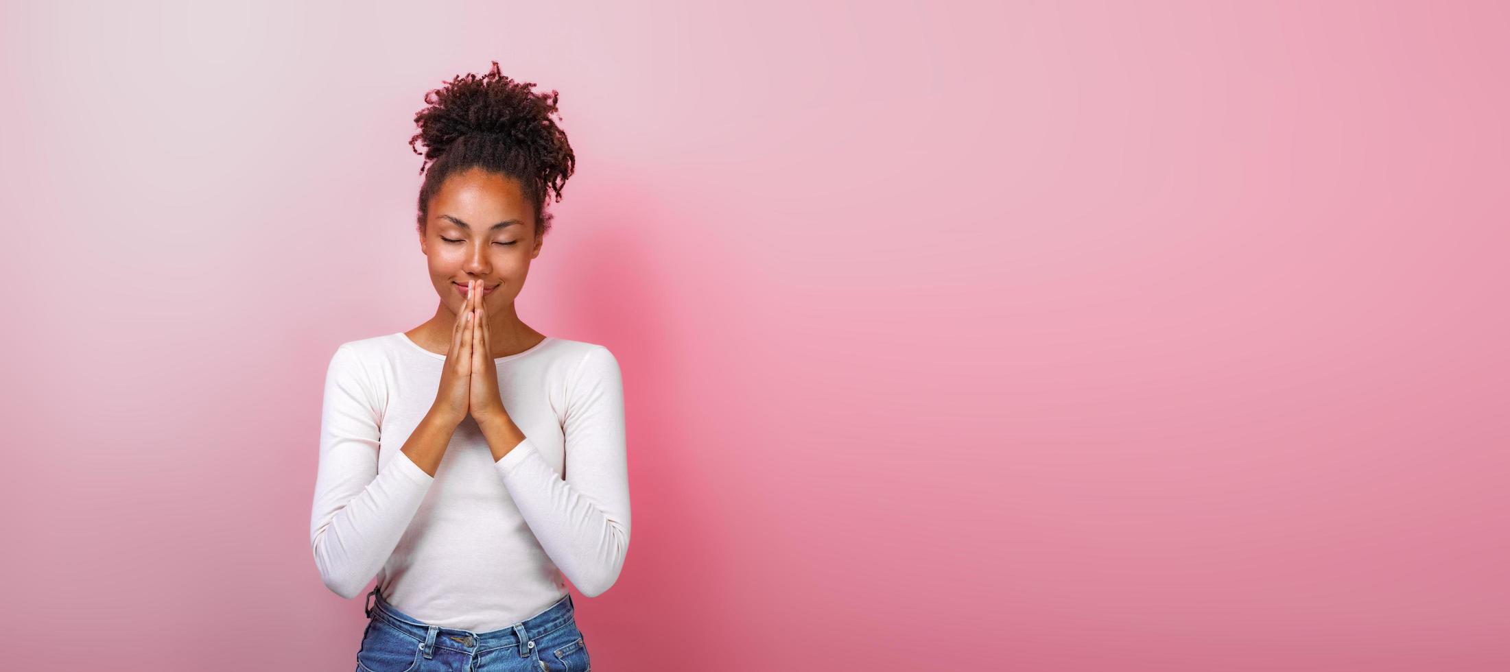 portrait de femme en supplication pose avec sourire et fermer les yeux sur fond rose. espace de copie photo