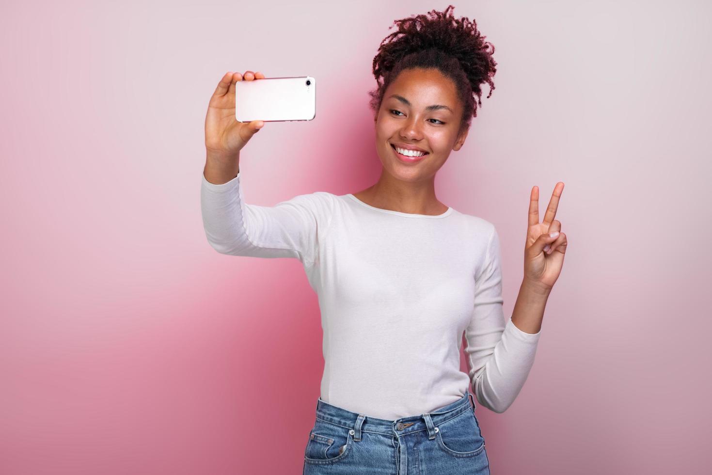 Jeune fille tenant un téléphone portable prend une photo avec un geste de victoire selfies - image