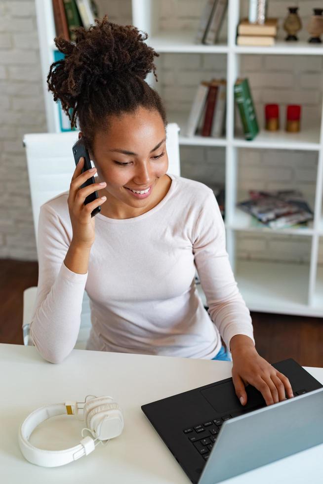 femme souriante travaillant sur ordinateur portable au bureau et parlant sur un smartphone. - image photo