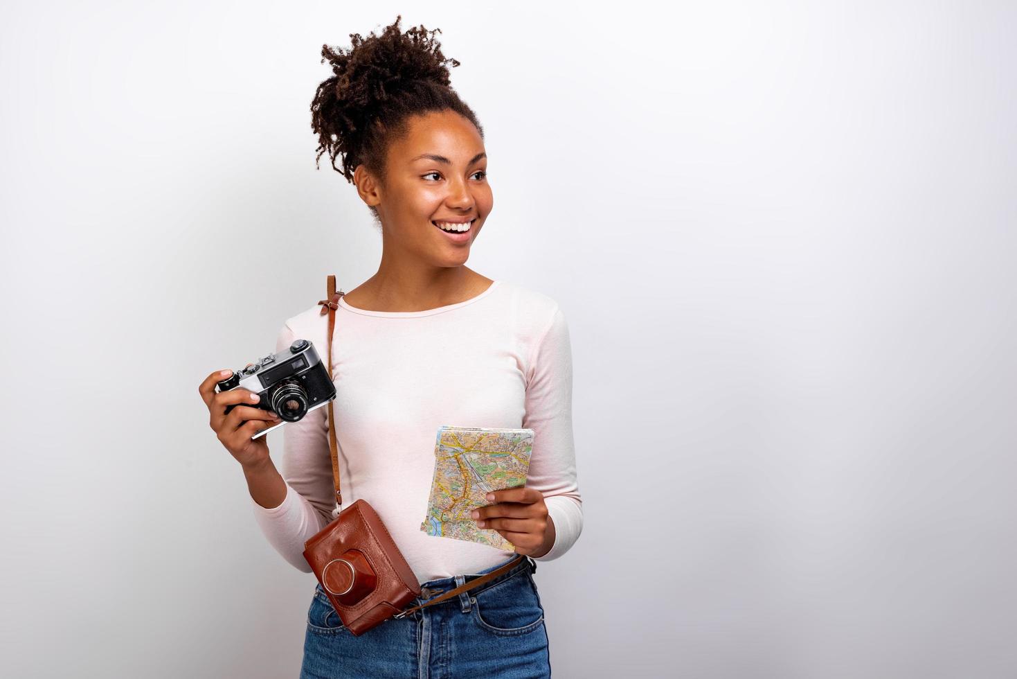 Portrait en studio d'une heureuse voyageuse mulâtre avec un appareil photo et une carte dans ses mains et regardant de côté- image