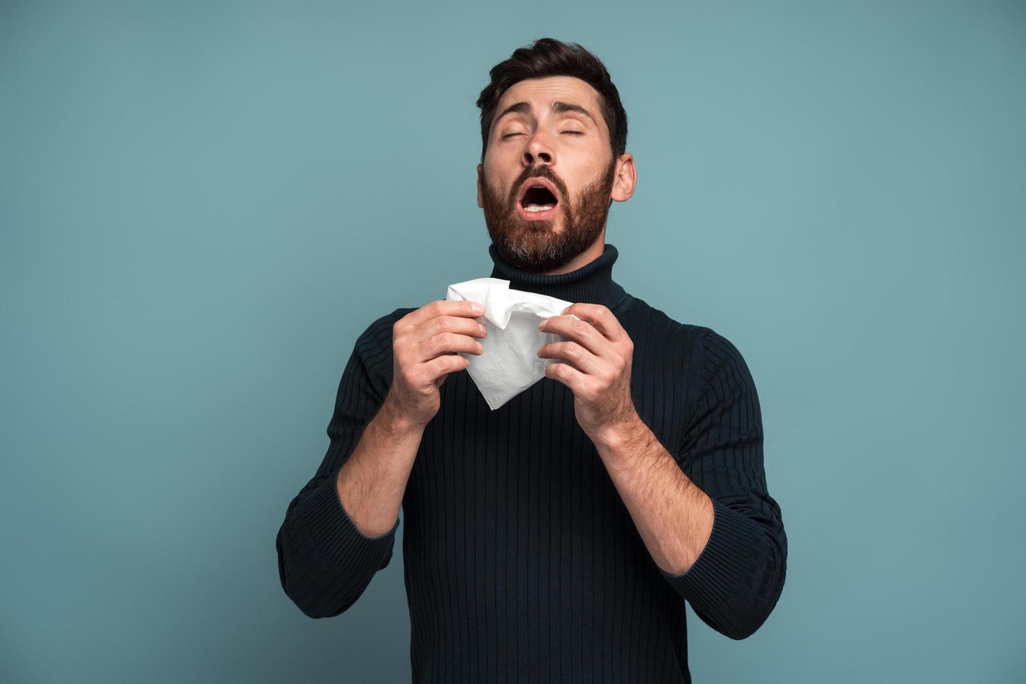 tousser ou éternuer. homme malade éternuant des tissus, toussant, se sentant mal, malade ou grippé, souffrant d'allergies ou de symptômes de grippe saisonnière. tourné en studio intérieur isolé sur fond bleu photo