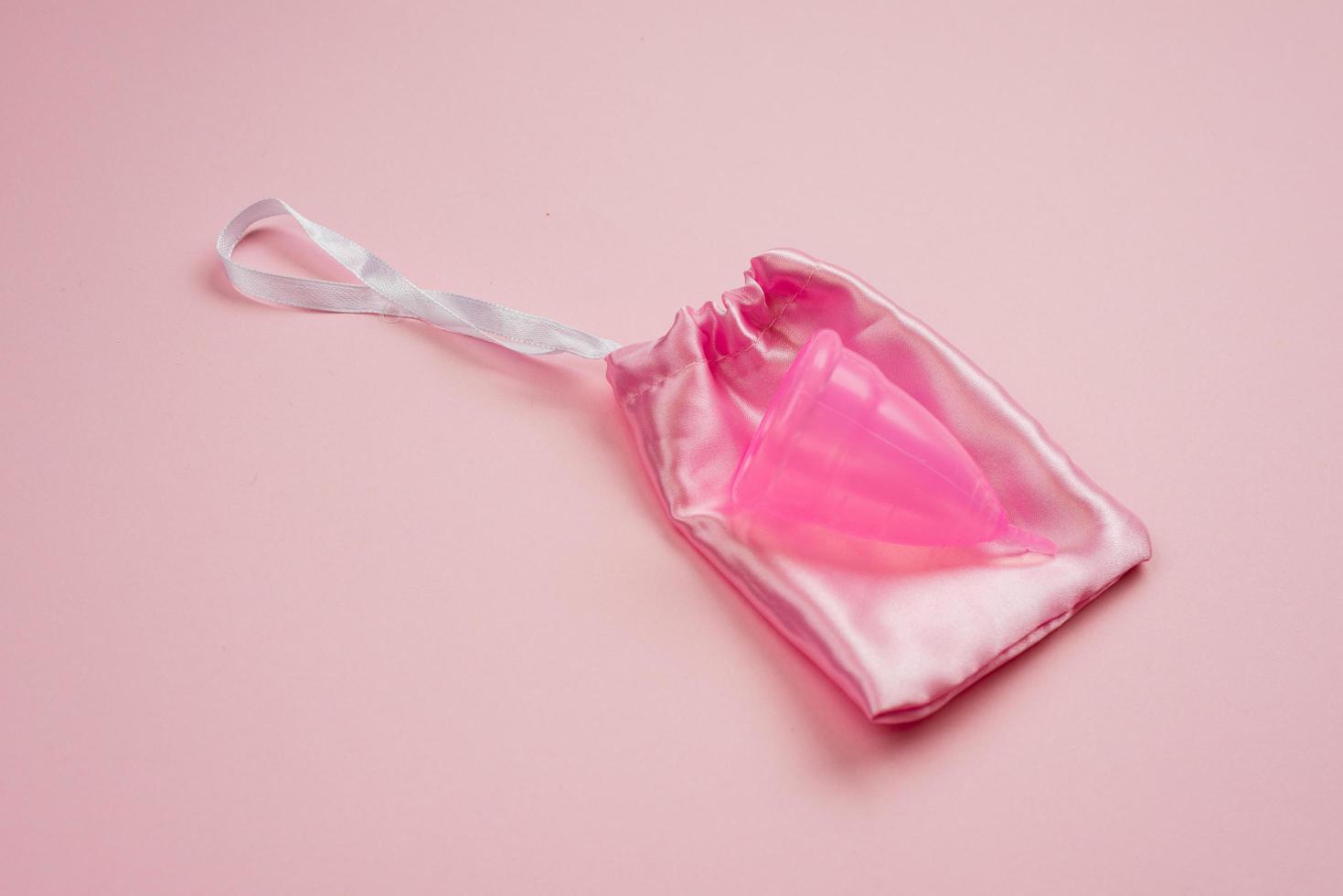 Coupe menstruelle en silicone allongée sur un sac en soie sur fond rose photo