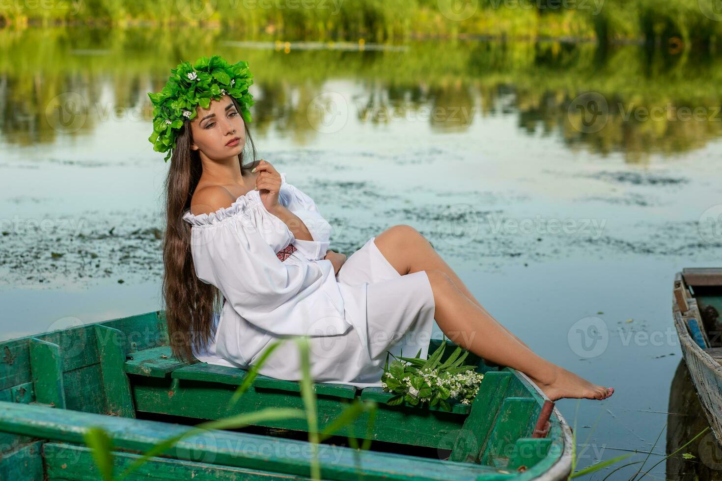 le nymphe avec longue foncé cheveux dans une blanc ancien robe séance dans une bateau dans le milieu de le rivière. photo