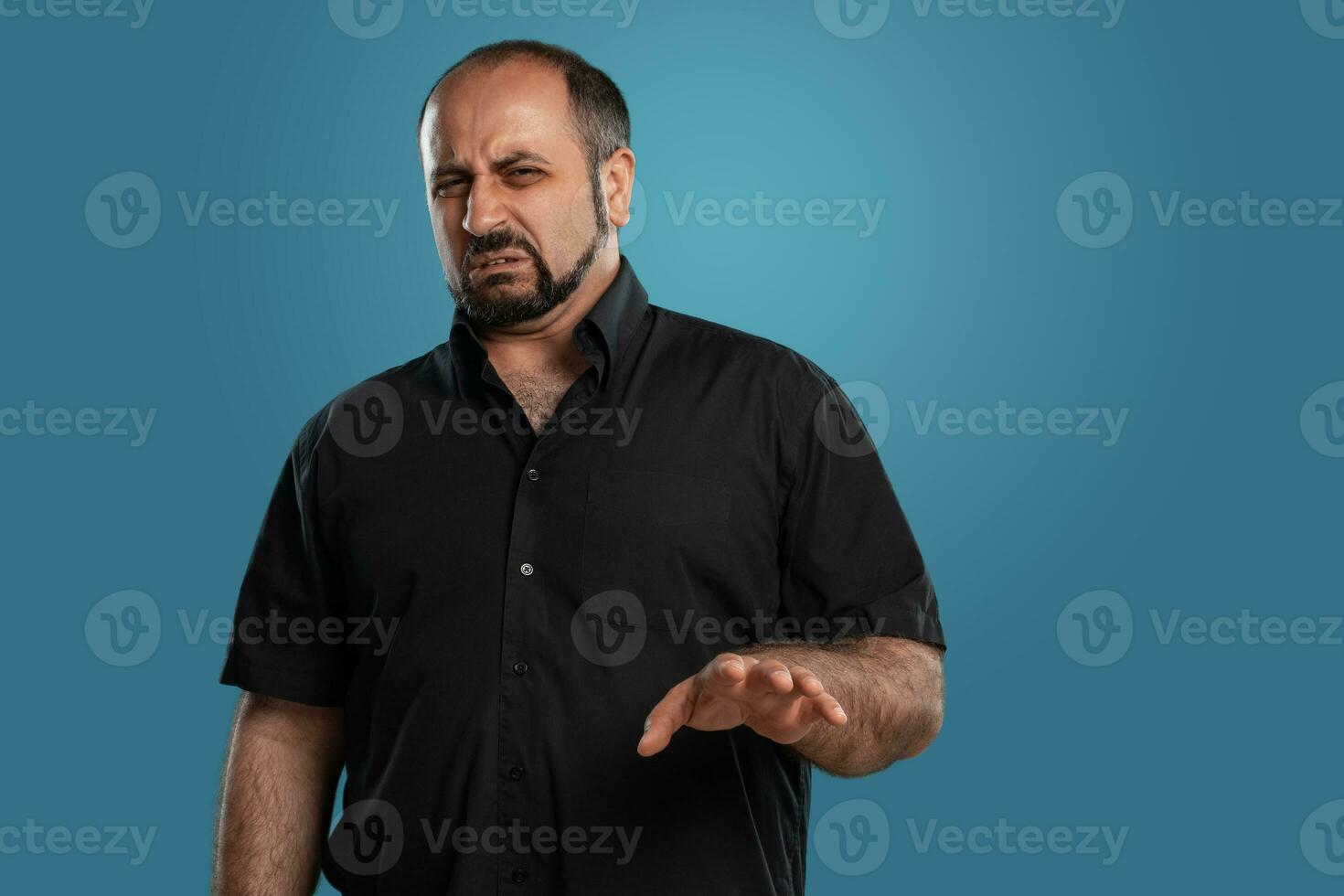 fermer portrait de une brunet âge moyen homme avec barbe, habillé dans une noir T-shirt et posant contre une bleu Contexte. photo