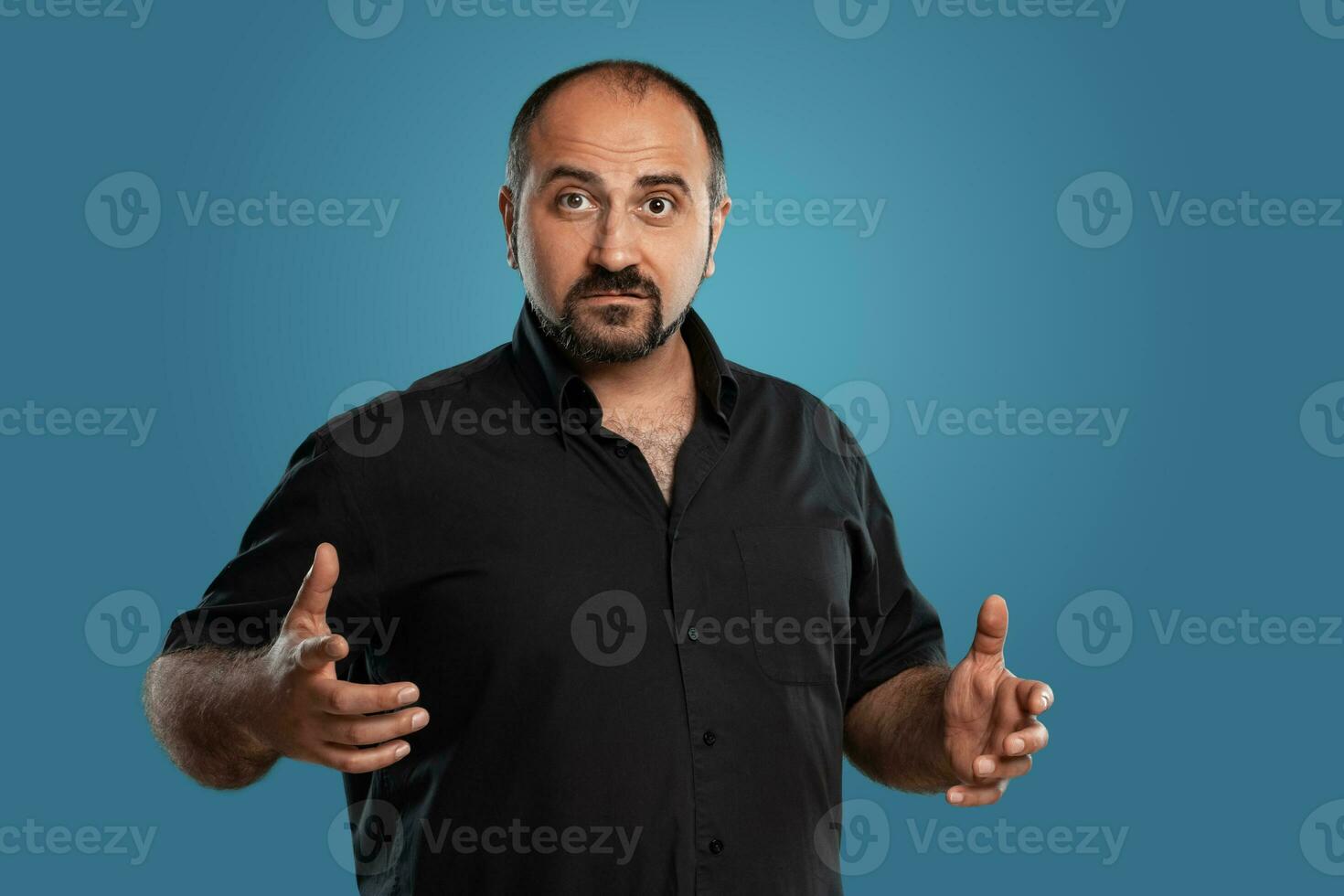 fermer portrait de une brunet âge moyen homme avec barbe, habillé dans une noir T-shirt et posant contre une bleu Contexte. photo