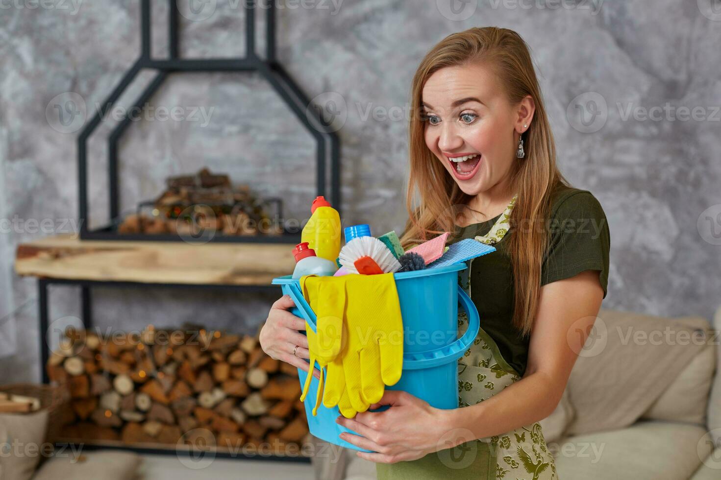 une nettoyage femme est permanent dans vivant pièce en portant une bleu seau rempli avec produits chimiques et installations pour ranger en haut dans sa main photo