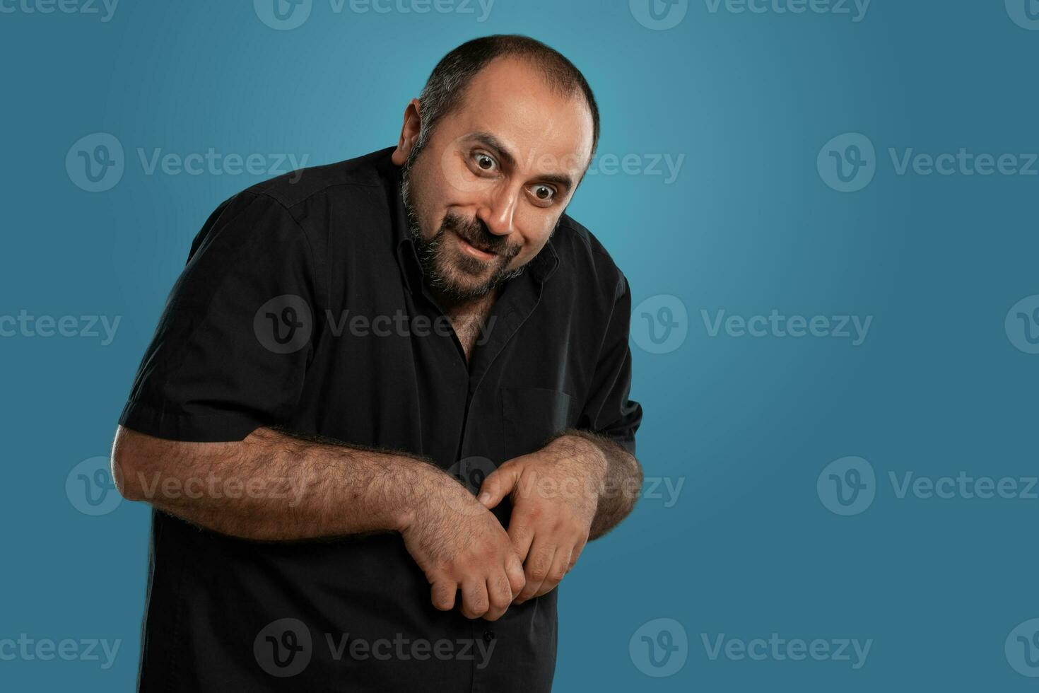 fermer portrait de une brunet âge moyen homme avec barbe, habillé dans une noir T-shirt et posant contre une bleu Contexte. photo