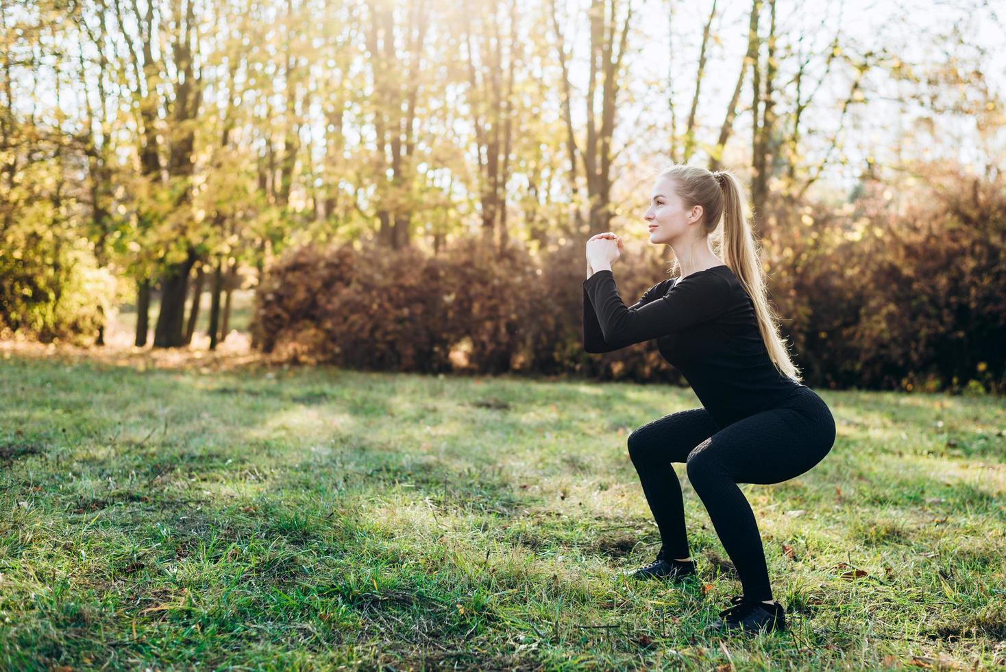 fille mince effectue des squats tout en faisant de l'exercice à l'extérieur photo