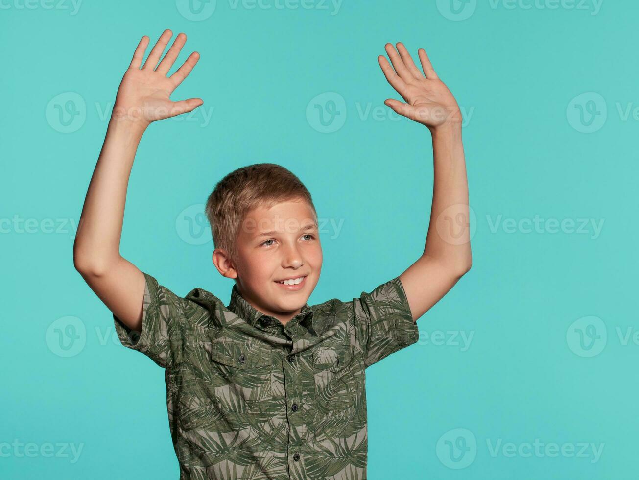 fermer portrait de une blond adolescent garçon dans une vert chemise avec paume impression posant contre une bleu studio Contexte. concept de sincère émotions. photo