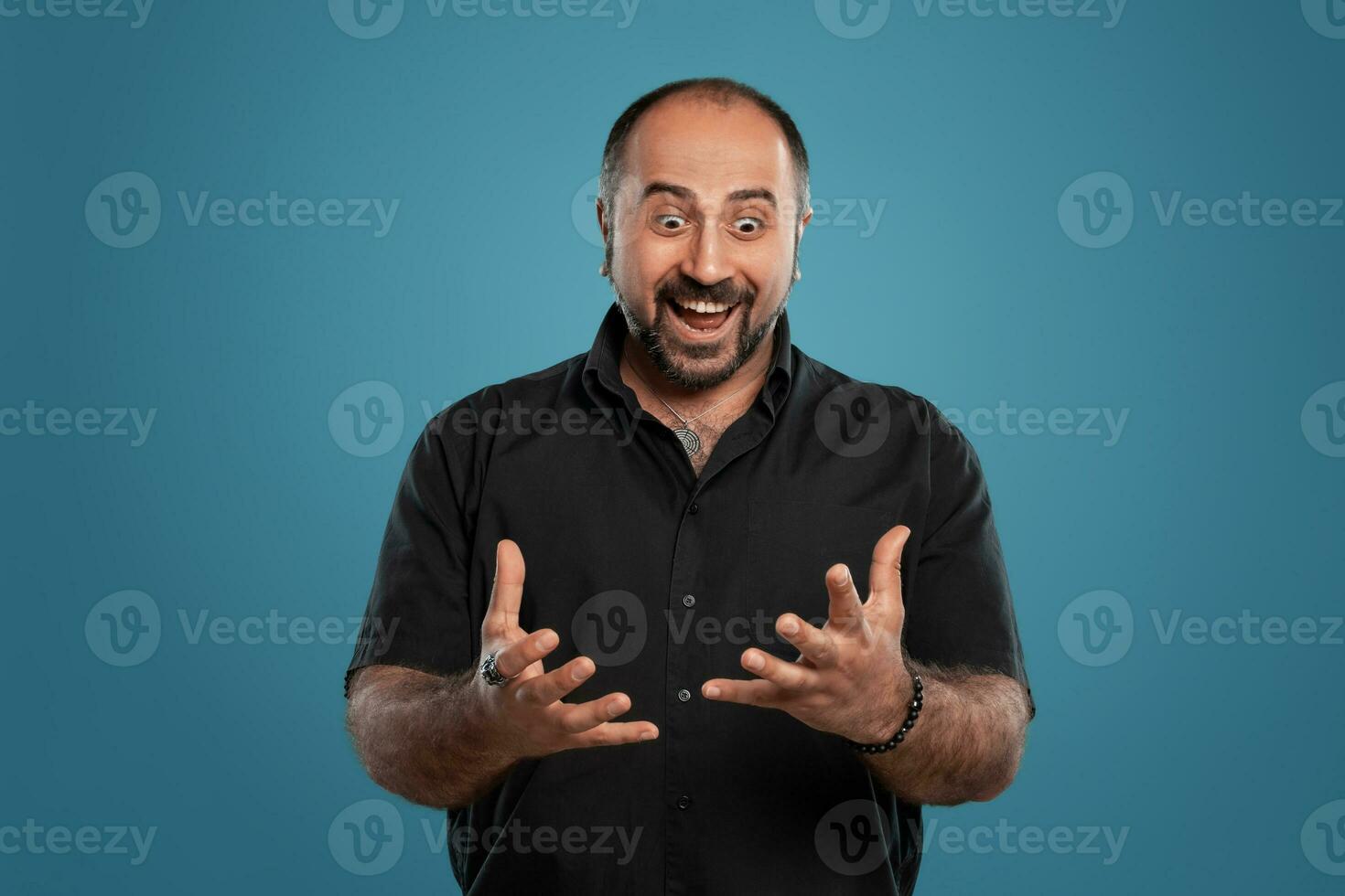 fermer portrait de une brunet âge moyen homme avec barbe, habillé dans une noir T-shirt et posant contre une bleu Contexte. photo