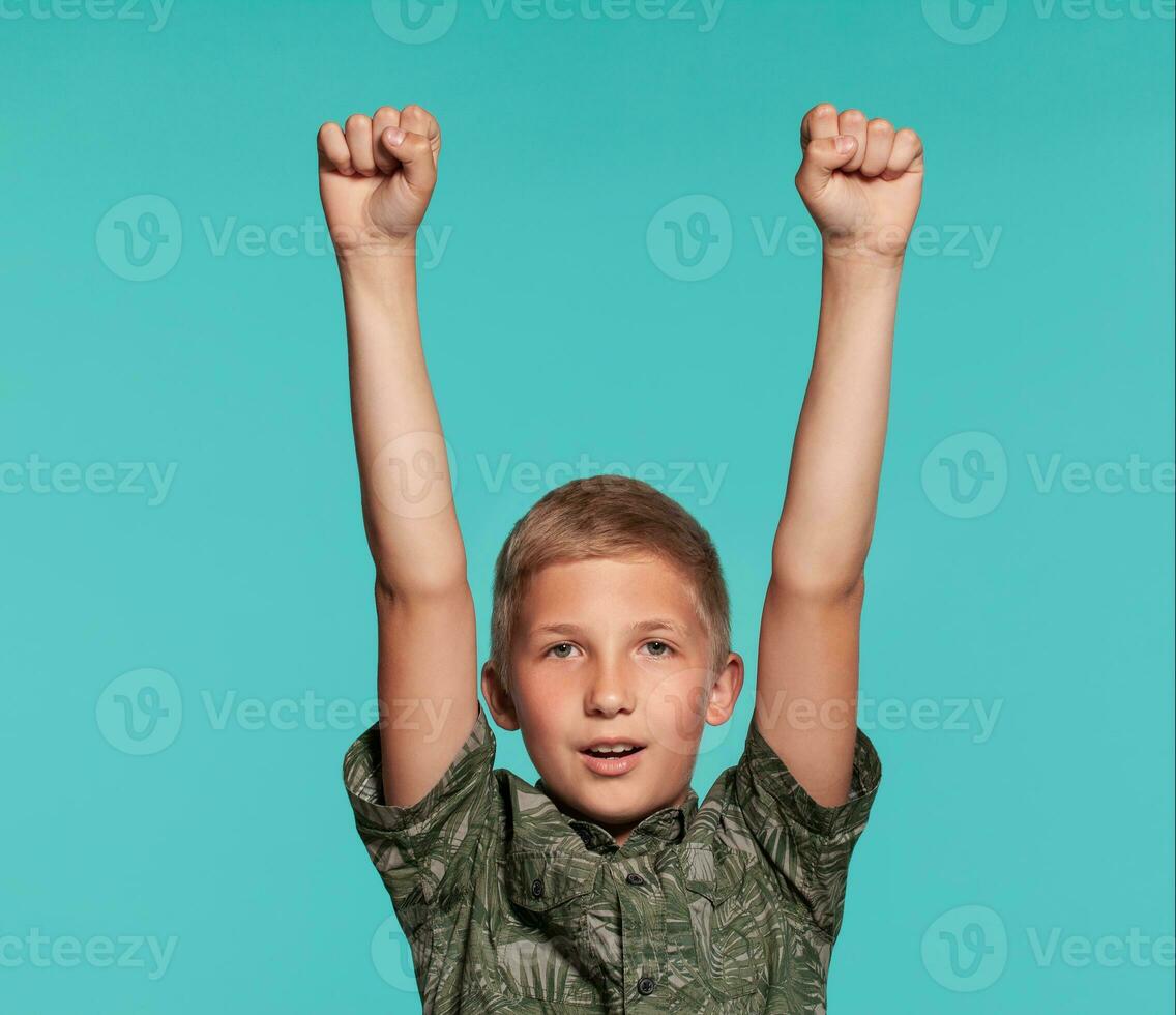 fermer portrait de une blond adolescent garçon dans une vert chemise avec paume impression posant contre une bleu studio Contexte. concept de sincère émotions. photo