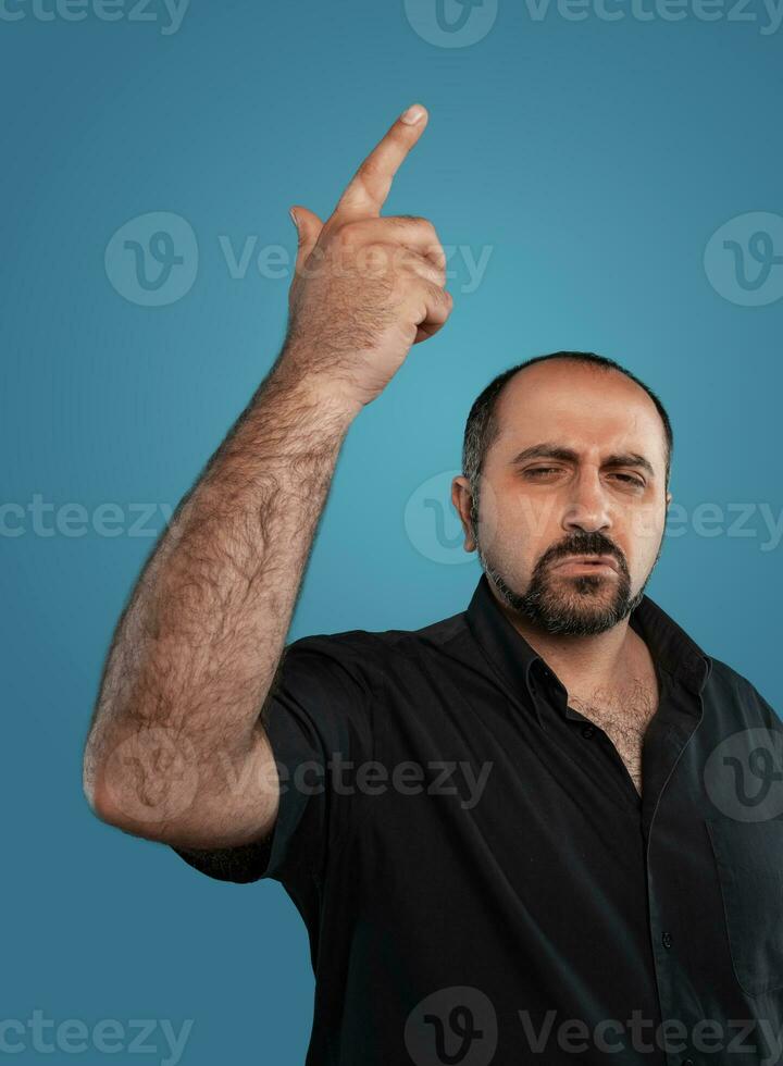 fermer portrait de une brunet âge moyen homme avec barbe, habillé dans une noir T-shirt et posant contre une bleu Contexte. photo
