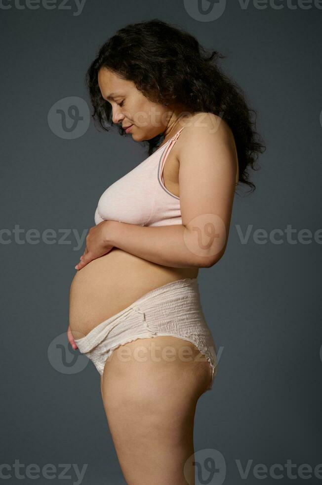 Nouveau lun dans sous-vêtement, spectacles sa post-partum ventre avec étendue Des marques et défauts, isolé gris. Publier grossesse. maternité photo