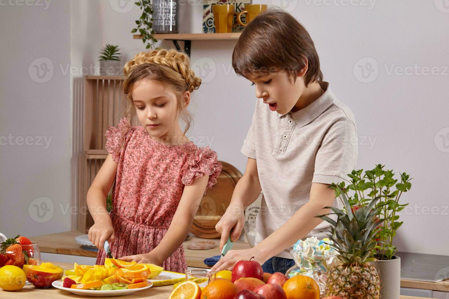 mignonne des gamins sont cuisine ensemble dans une cuisine contre une blanc mur avec étagères sur il. photo