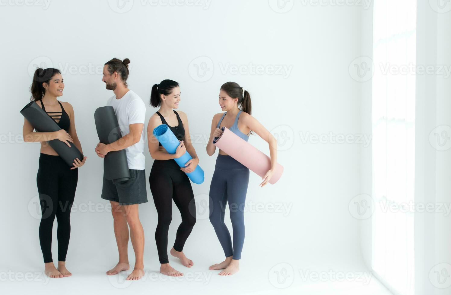 une groupe de femelle et Masculin les athlètes se tenait et bavardé à l'amiable dans le studio avant début avec le yoga classe. photo