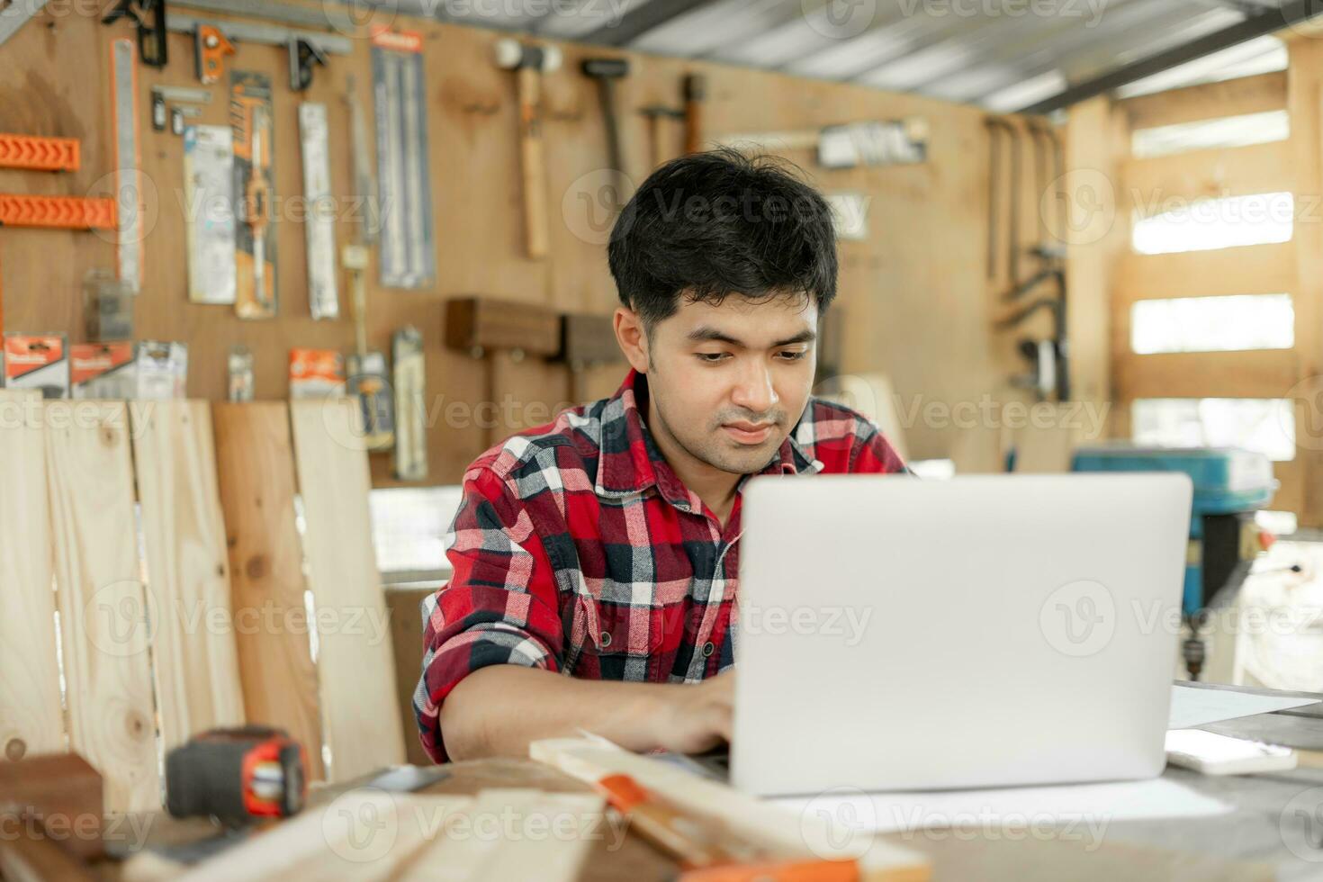 asiatique homme propriétaire une petit meubles affaires est revérifier commande en ligne. Charpentier Masculin est régler bois à le voulu taille. architecte, designer, intégré, professionnel bois, artisan, atelier. photo