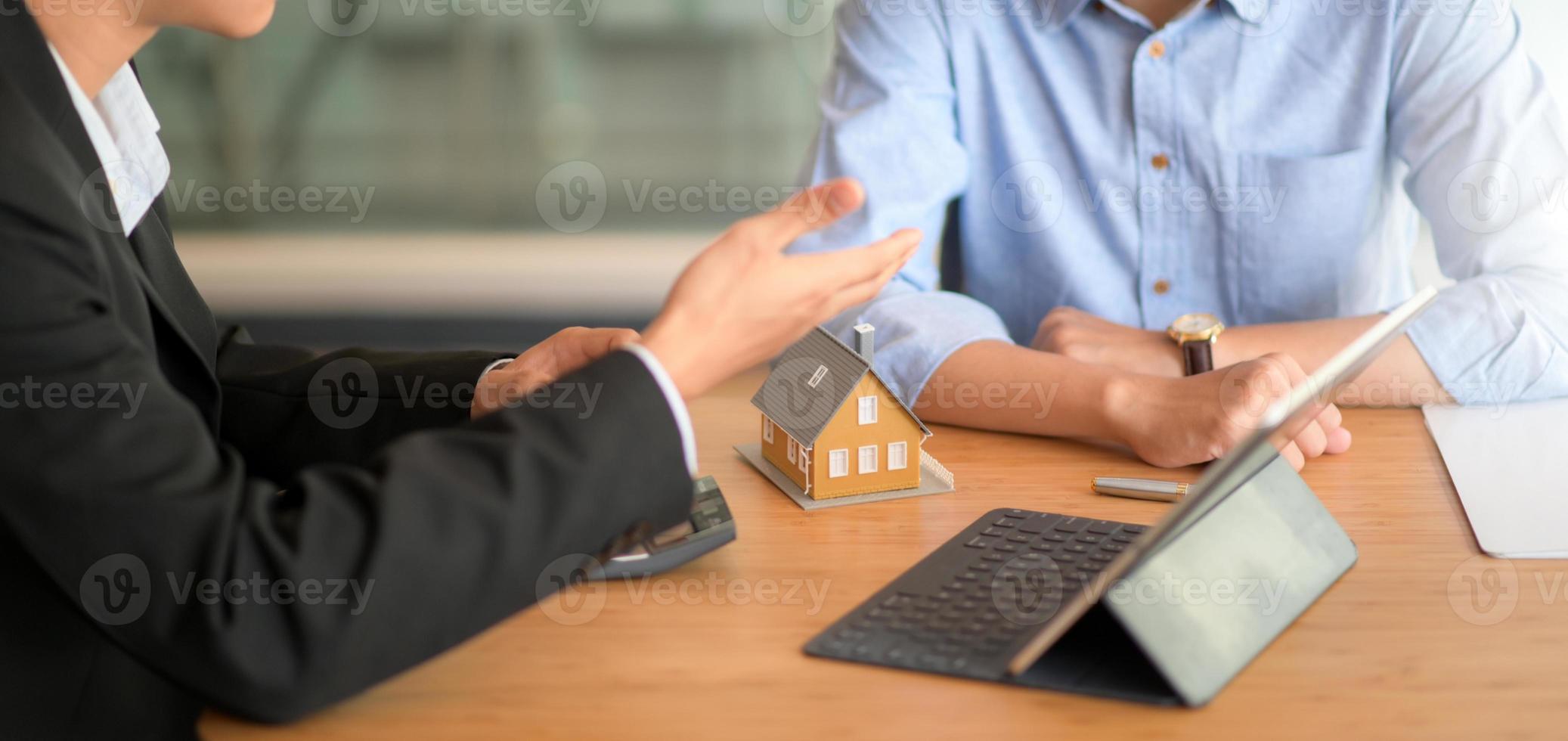 L'agent d'assurance recommande des forfaits d'assurance immobilière aux clients avec des tablettes et un modèle de maison. photo