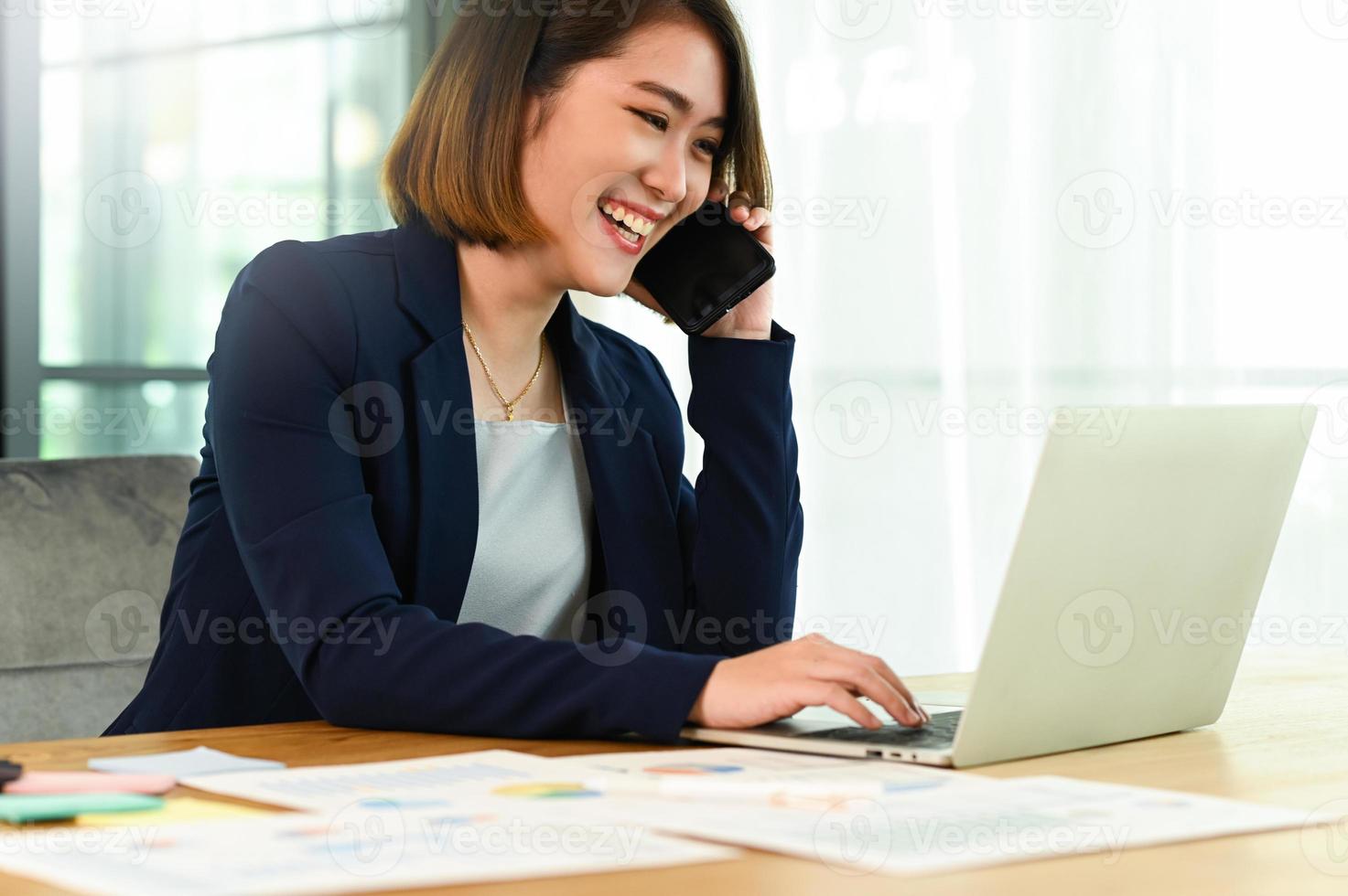 femme d'affaires portant un costume parlant au téléphone et utilisant un visage souriant d'ordinateur portable photo