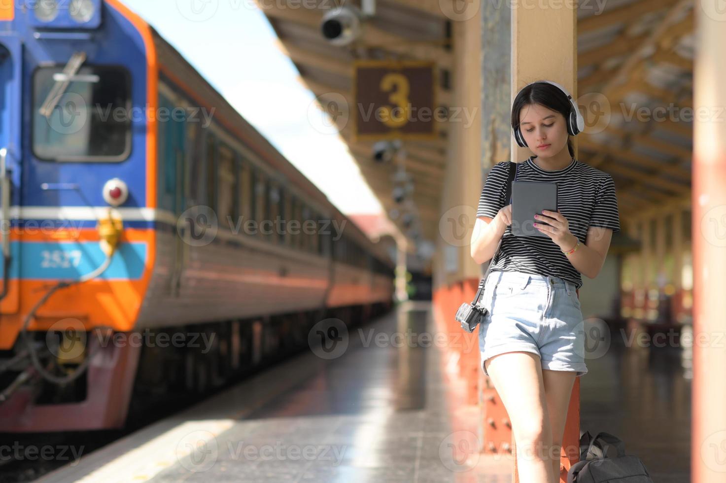 une adolescente portant des écouteurs écoutant de la musique à partir d'une application sur sa tablette en attendant un train. photo