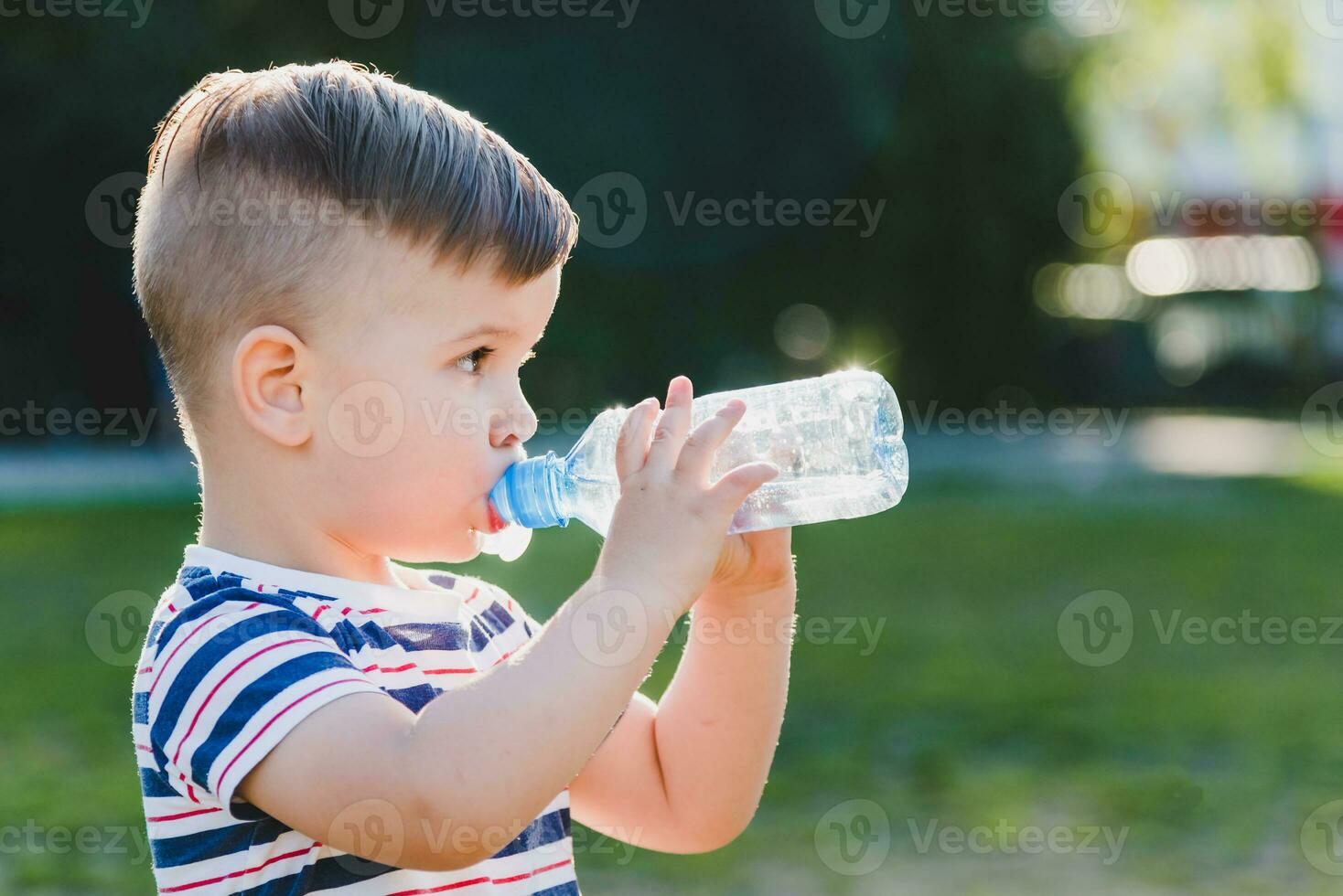 Beau garçon les boissons clair l'eau de une bouteille sur une ensoleillé journée à l'extérieur photo