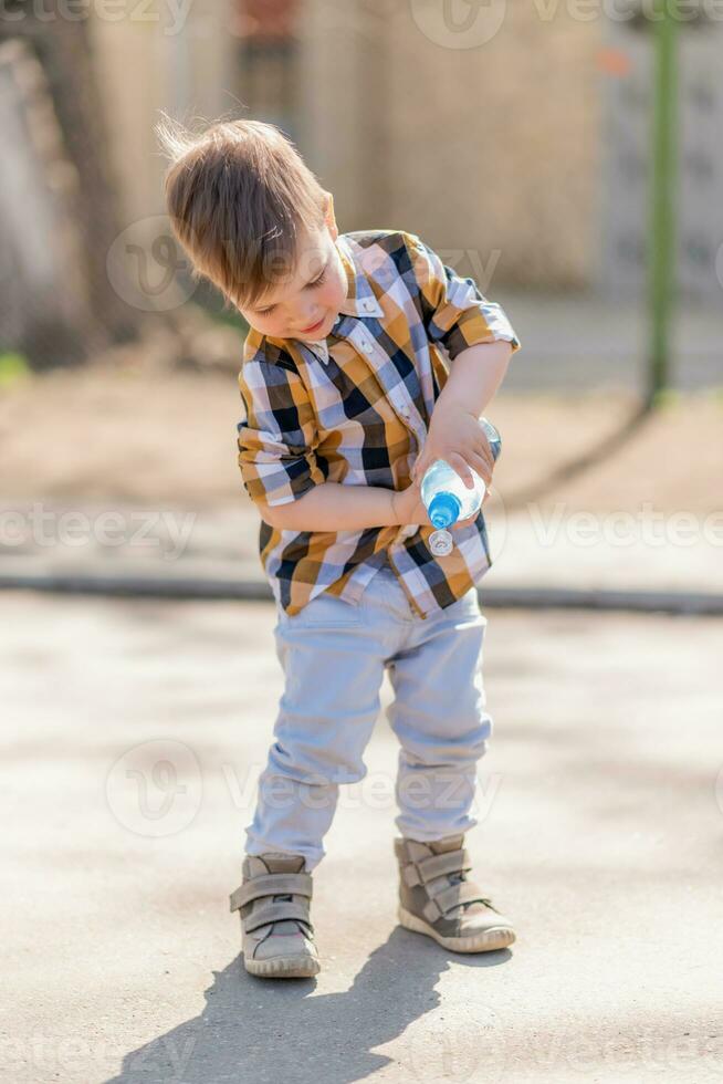 magnifique enfant verse l'eau de une bouteille sur le sol photo