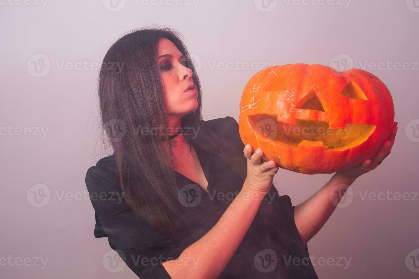 femme comme sorcière est permanent avec le citrouille dans le studio. Halloween et carnaval concept photo