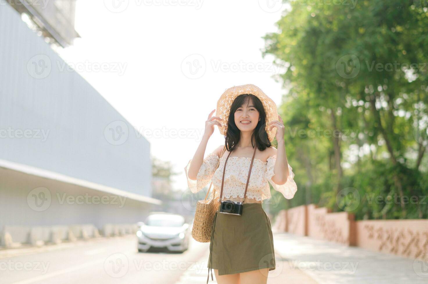 portrait de asiatique Jeune femme voyageur avec tissage chapeau et panier et une caméra permanent par le rue. périple voyage mode de vie, monde Voyage explorateur ou Asie été tourisme concept. photo