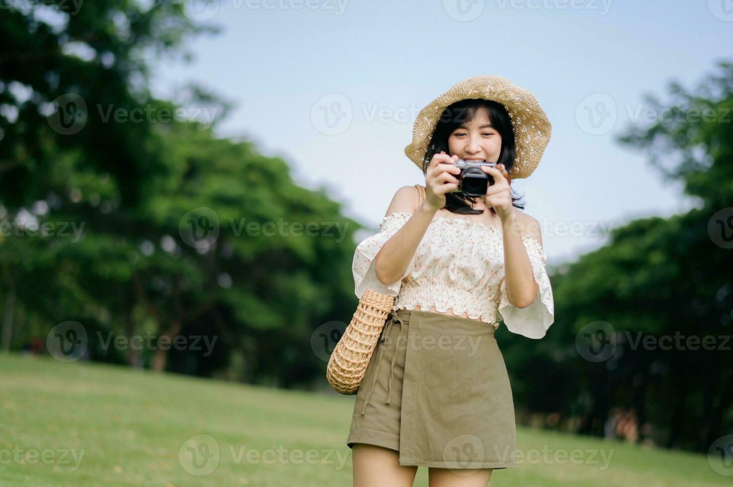 portrait de asiatique Jeune femme voyageur avec tissage chapeau et panier et une caméra sur vert Publique parc la nature Contexte. périple voyage mode de vie, monde Voyage explorateur ou Asie été tourisme concept. photo