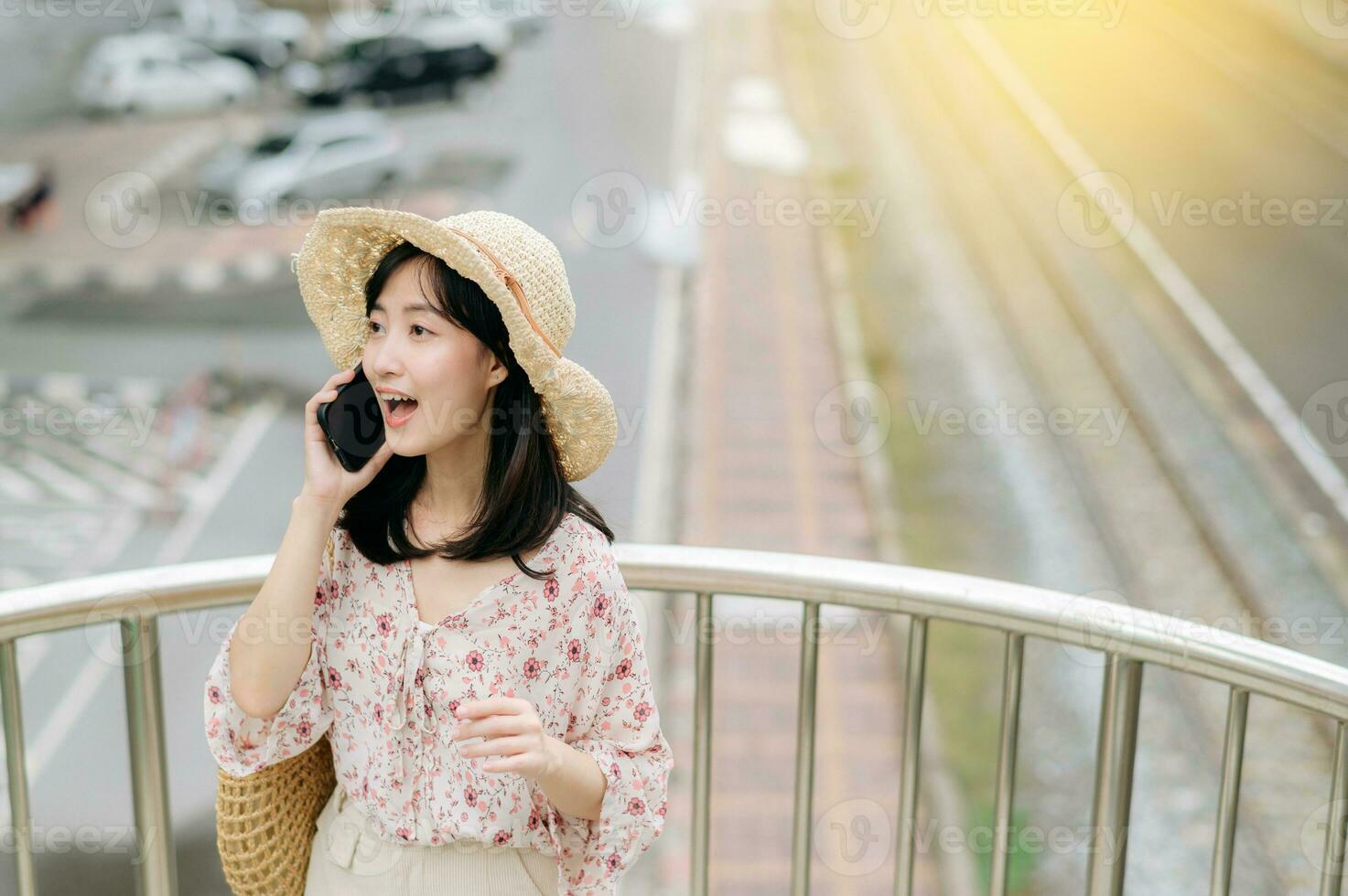 Jeune asiatique femme voyageur avec tissage panier en utilisant mobile téléphone et permanent sur dépasser avec chemin de fer Contexte. périple voyage mode de vie, monde Voyage explorateur ou Asie été tourisme concept. photo