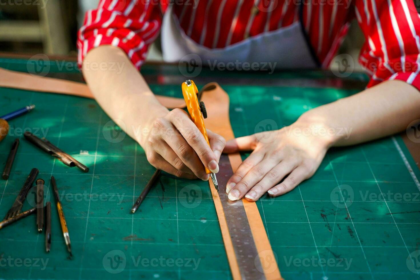 fermer et surgir mains de cuir fabricant en utilisant une coupeur couteau à Couper une pièce de cuir feuille selon à le conception à apporter en dehors à Coudre dans des produits pour clients. photo
