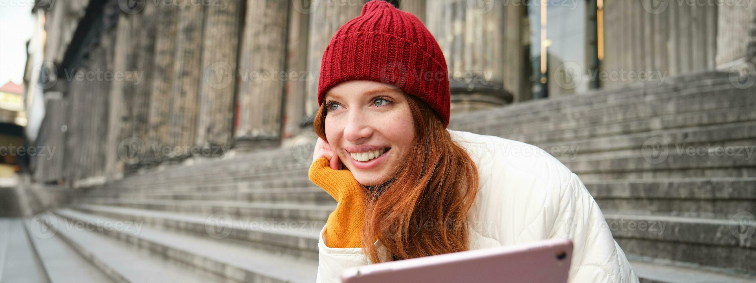 Extérieur coup de Jeune élégant roux fille est assis sur escalier et connecte à Publique Wifi, les usages numérique tablette, lit nouvelles sur gadget photo