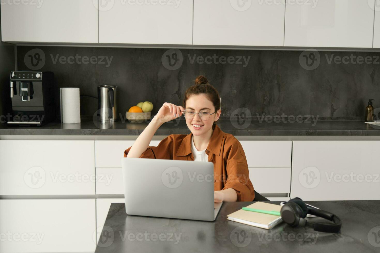 portrait de Jeune femme, affaires propriétaire dans lunettes, séance avec portable dans cuisine, travail de maison. étudiant en étudiant, Faire devoirs sur ordinateur photo