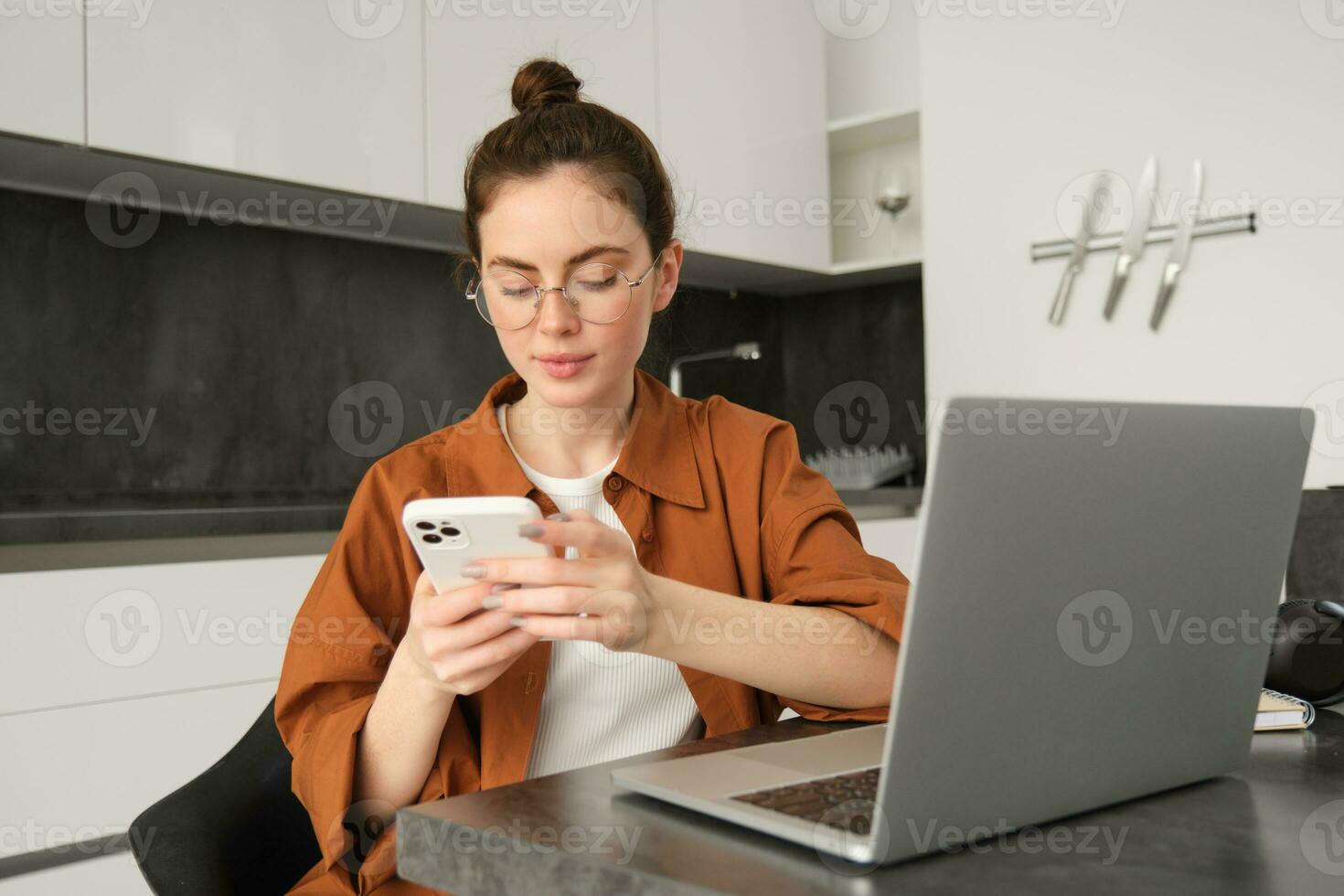 portrait de Jeune femelle pigiste, femme travail de Accueil avec ordinateur portable, fille programmeur séance avec ordinateur dans cuisine, répondre message sur téléphone intelligent photo