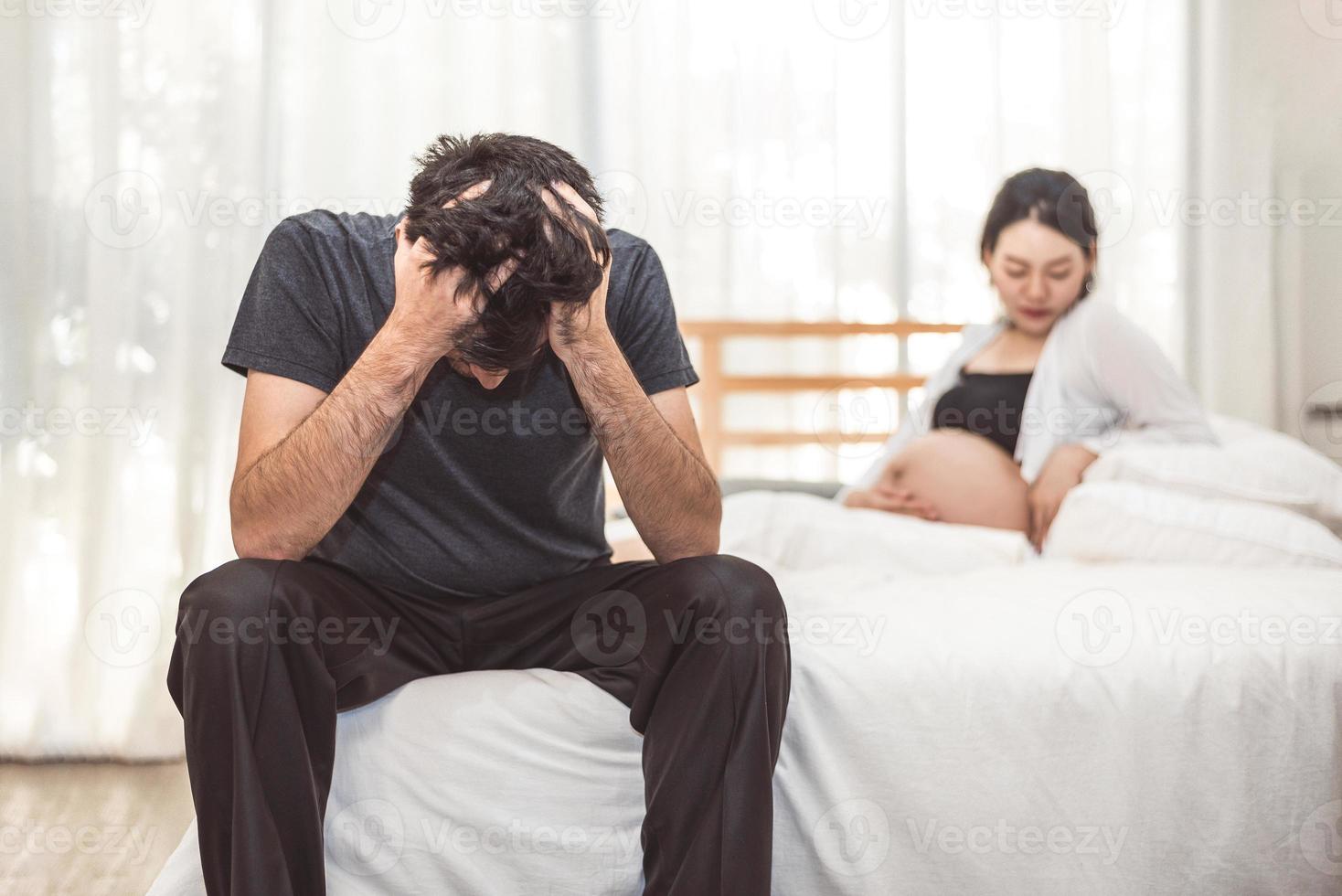 homme de stress inquiet assis sur le lit avec la main sur le front dans la chambre dans une émotion d'humeur sérieuse avec fond de femme enceinte femme. trouble dépressif majeur appelé concept mdd. soins de santé physique photo