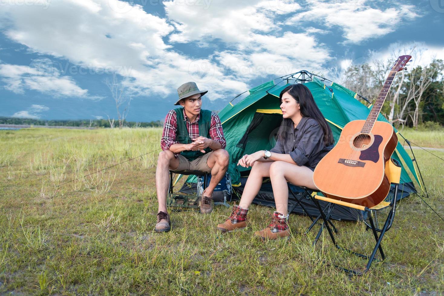 deux personnes parlant près d'une tente de camping dans un champ de prairie. voyageur masculin et féminin regardant le point de vue de l'attraction. couples aventure à l'extérieur ensemble. concept de personnes et de modes de vie photo
