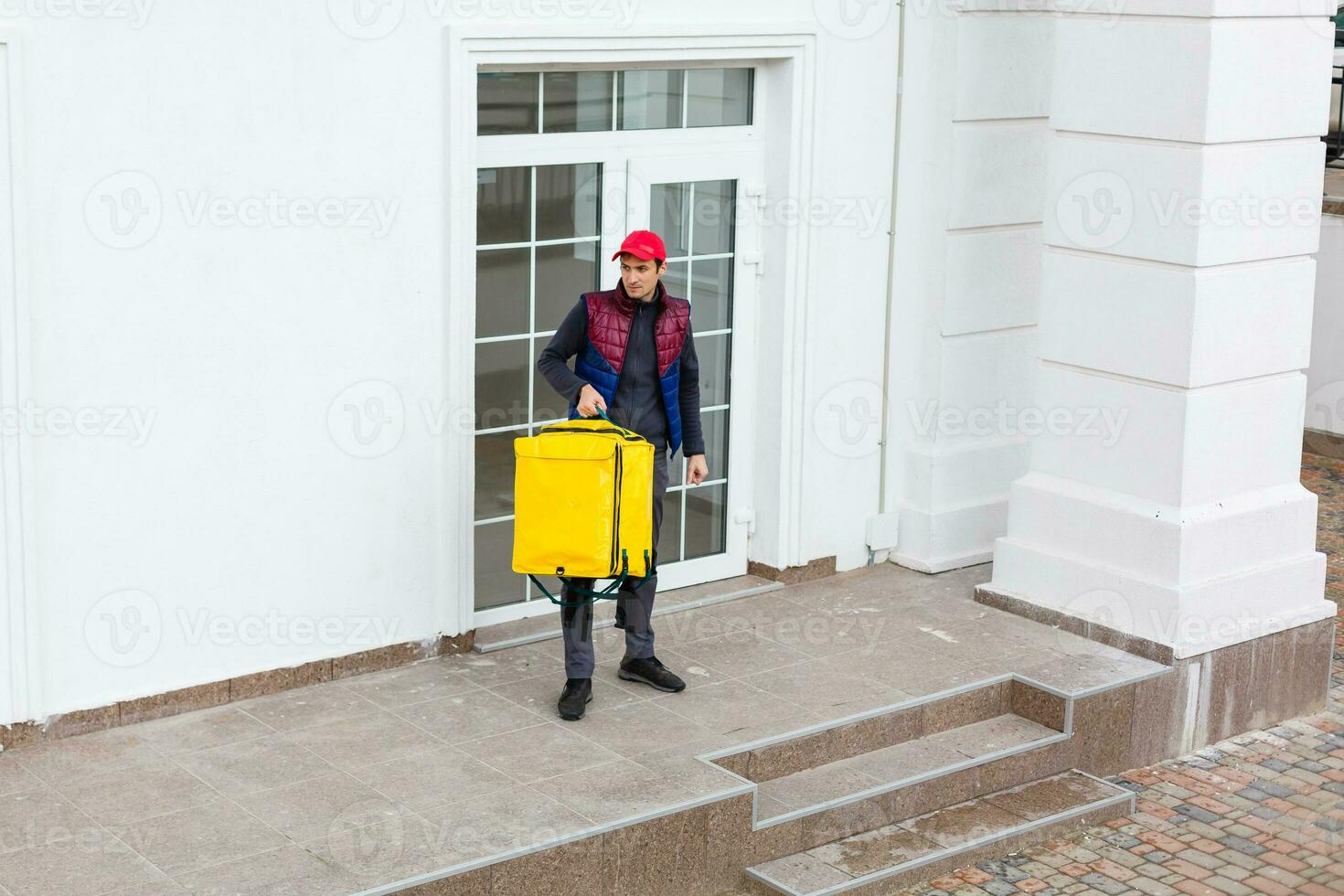 portrait de une de bonne humeur livraison homme permanent avec Jaune thermo sac à dos pour nourriture livraison sur le rue en plein air photo