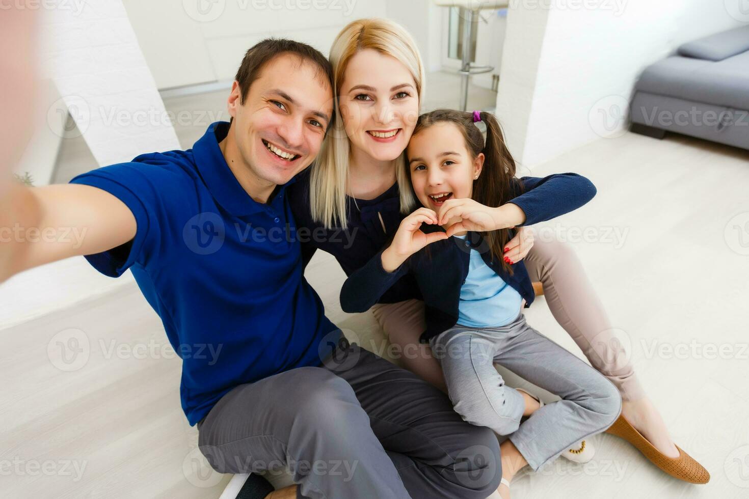 magnifique Jeune mère, père et leur fille sont fabrication selfie en utilisant une téléphone et souriant tandis que séance à Accueil photo