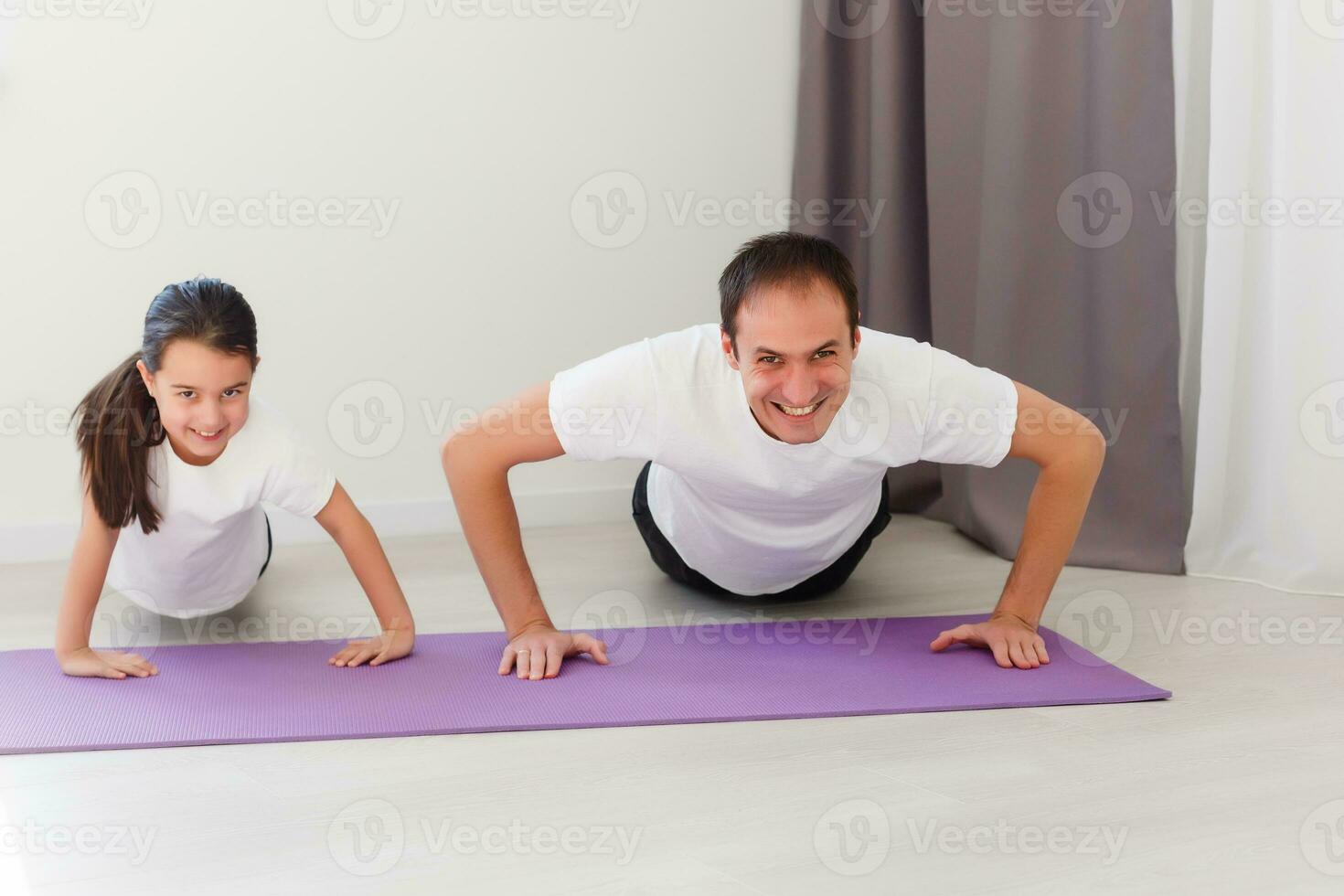 Beau Jeune père et le sien mignonne peu fille sont Faire révérer planche avec jambe élever sur le sol à maison. famille aptitude entraînement. photo