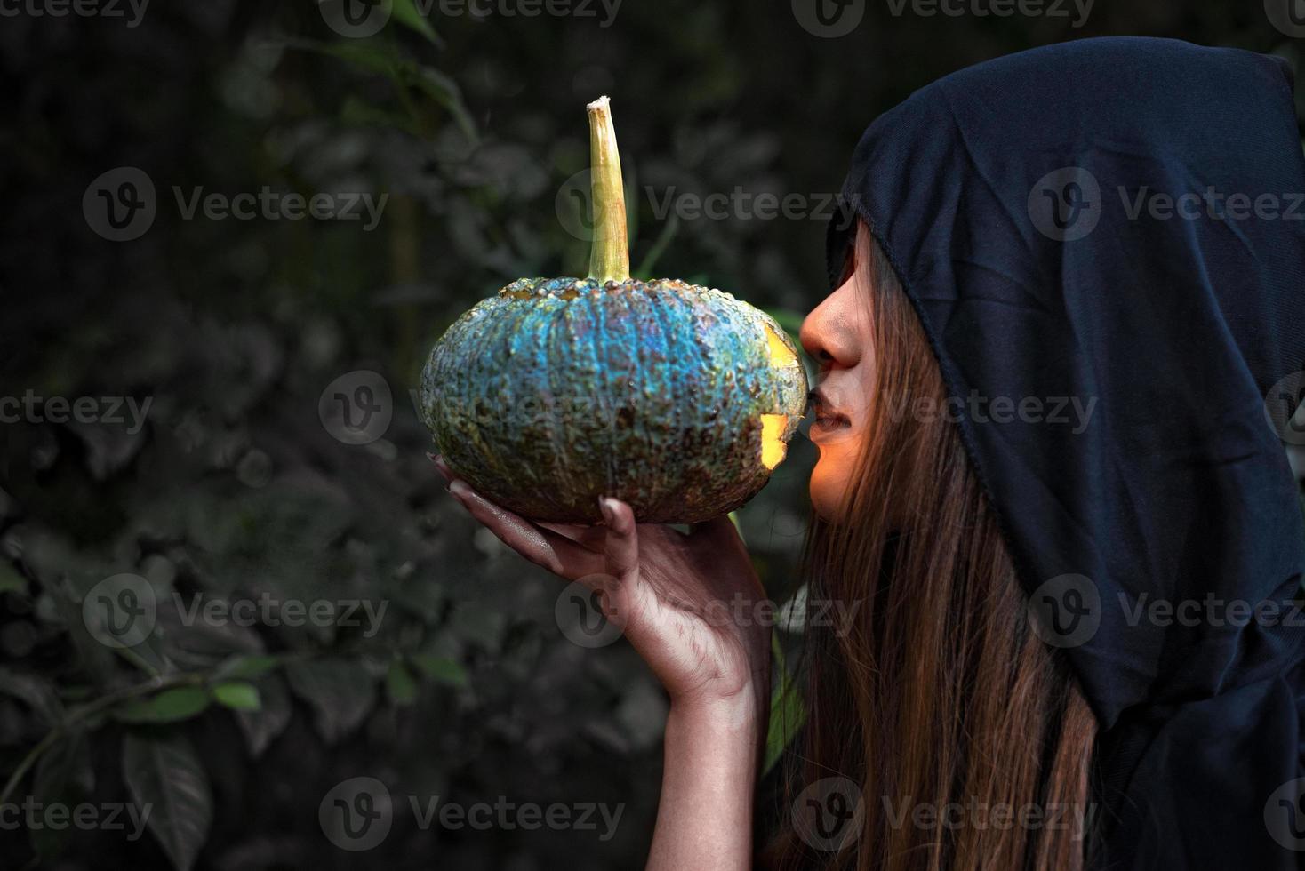 sorciere embrassant la lanterne de citrouille. costume féminin en vêtements noirs et capuche sur fond de forêt mystérieuse. concept de jour et de mystère d'halloween. fantaisie de thème magique. concept de vie après la mort et de mort photo