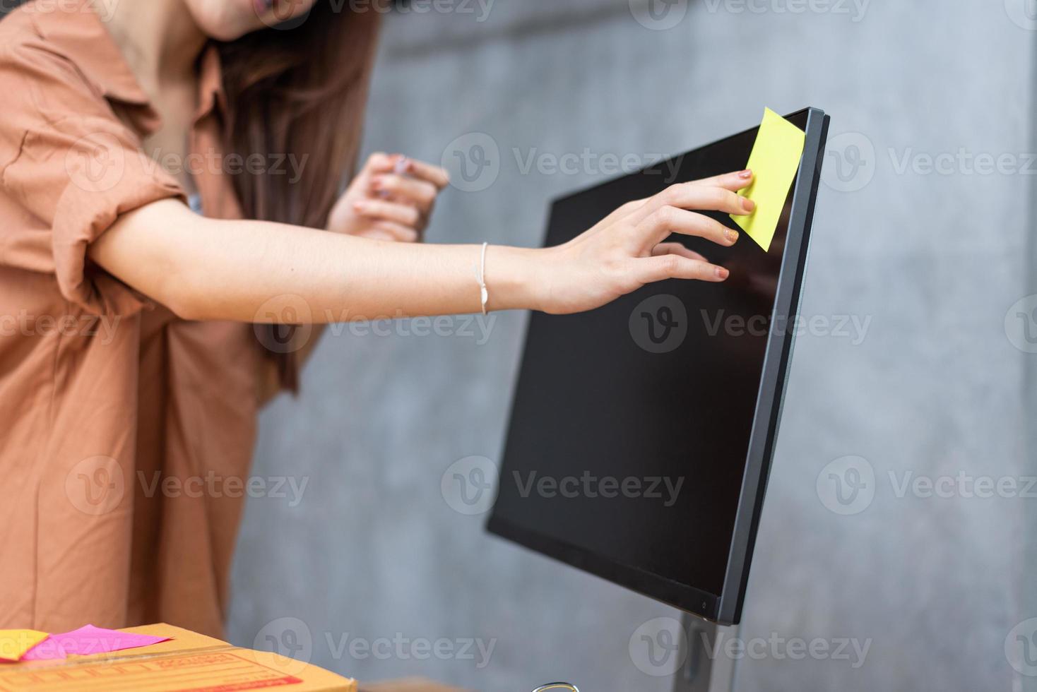 femme d'affaires collant un mémo de liste de commandes sur un écran d'ordinateur pour rappeler d'envoyer des colis aux clients. concept d'entreprise et de service. thème des achats en ligne et des petits entrepreneurs photo