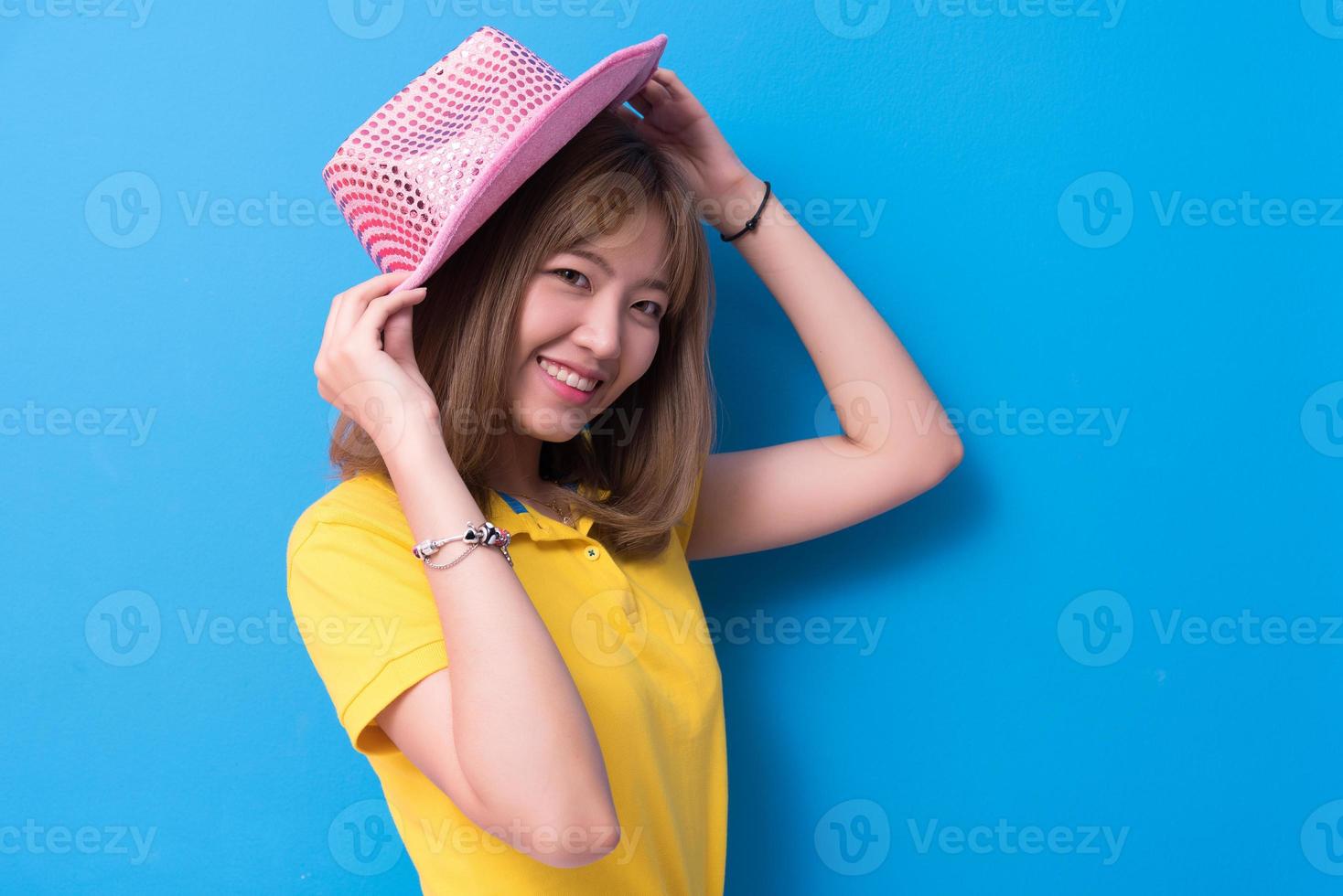 femme de beauté posant avec un chapeau rose devant un fond de mur bleu. concept d'été et vintage. style de vie de bonheur et thème de portrait de personnes. geste mignon et ton pastel photo