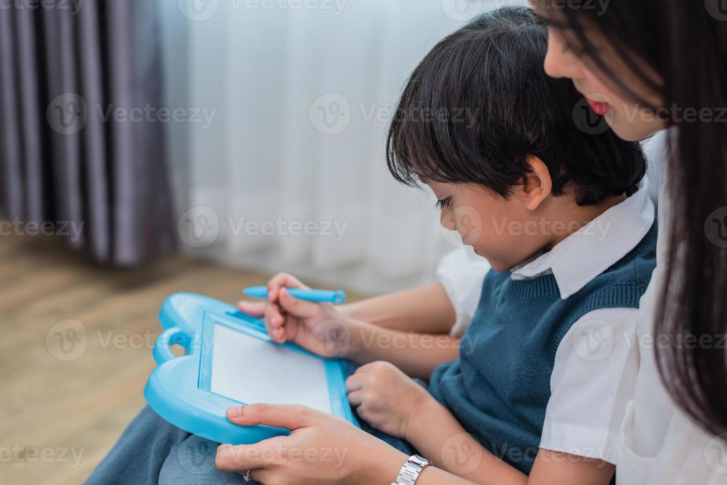 maman asiatique enseigne à un garçon mignon à dessiner ensemble au tableau. retour à l'école et concept d'éducation. thème de la famille et de la maison douce. thème des enfants d'âge préscolaire photo