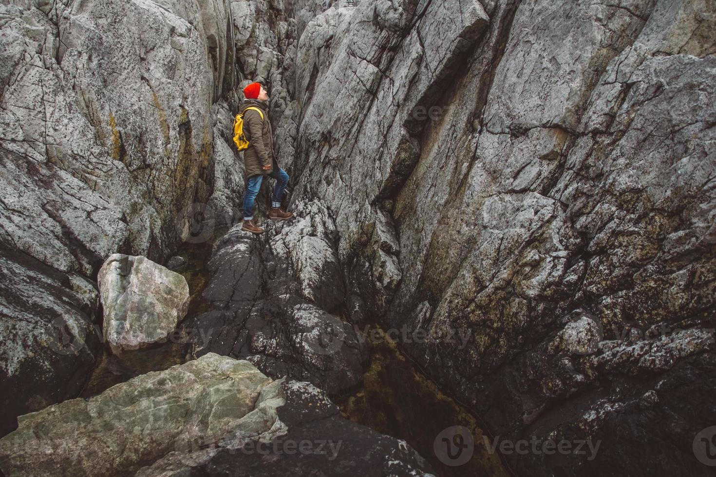 homme voyageur avec un sac à dos jaune portant un chapeau rouge debout sur le fond des rochers. concept de mode de vie de voyage photo