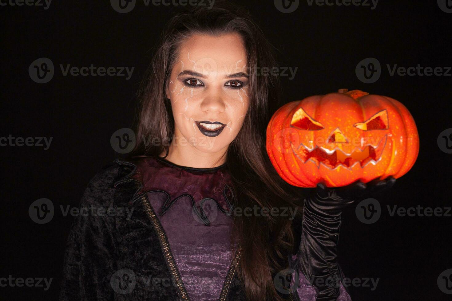 Dame dans sorcière costume en portant une citrouille plus de noir Contexte pour Halloween. photo