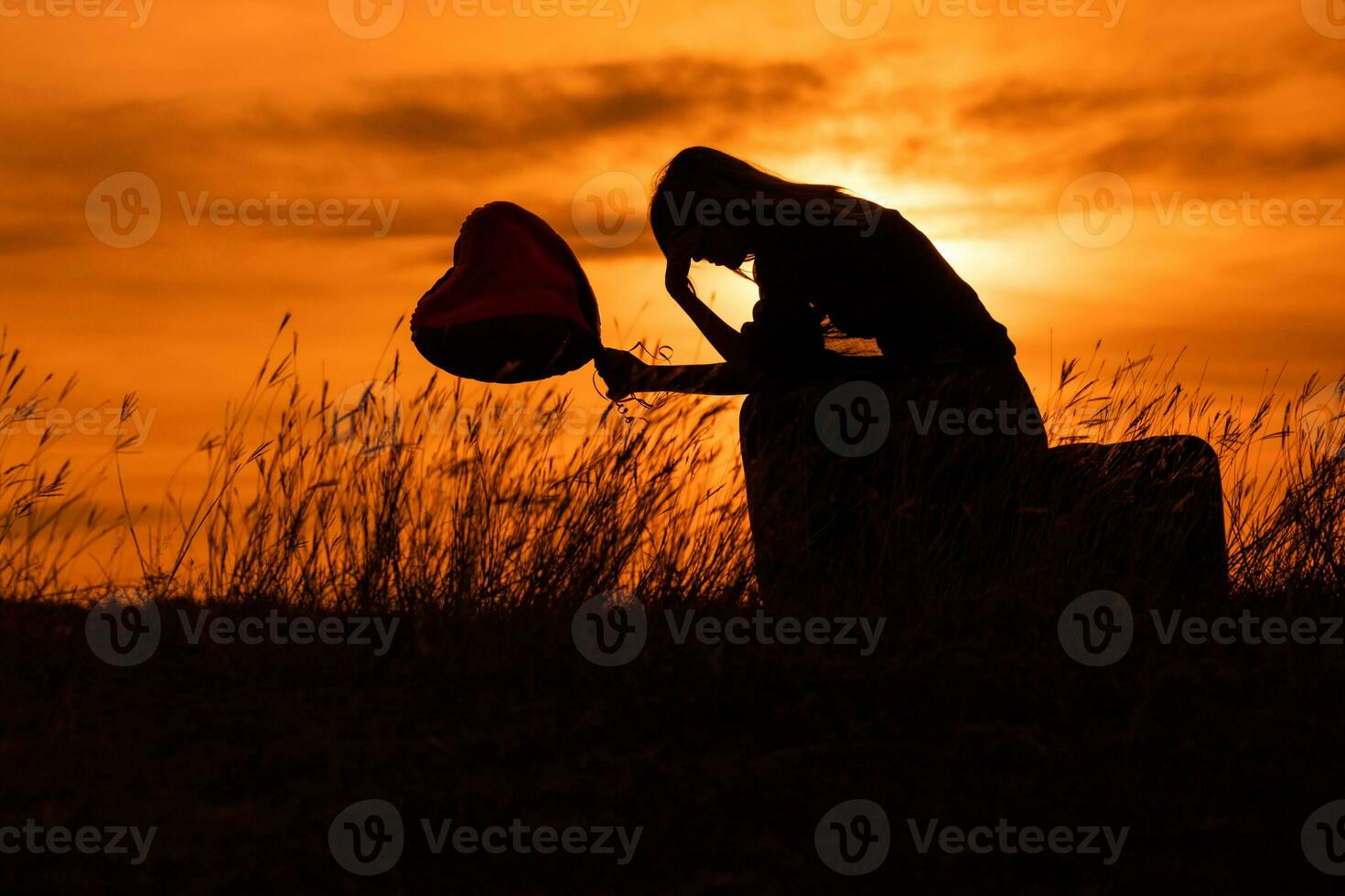 silhouette de une triste femme séance sur valise avec cœur en forme de ballon à le le coucher du soleil. photo