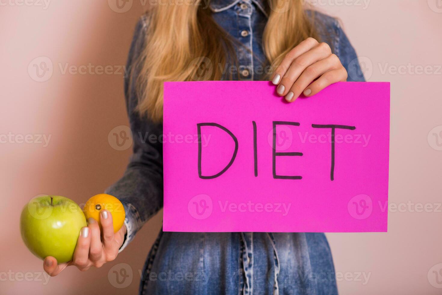 femme en portant papier avec mot régime et fruit tandis que permanent dans de face de mur. photo
