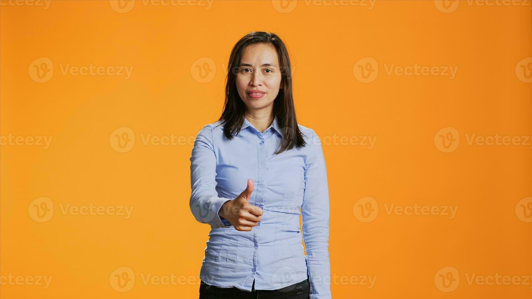 philippin la personne montrant les pouces en haut signe sur caméra, exprimer bien ambiance et positivité plus de Orange Contexte. Jeune souriant femme donnant comme dans studio, en présentant approbation geste. photo