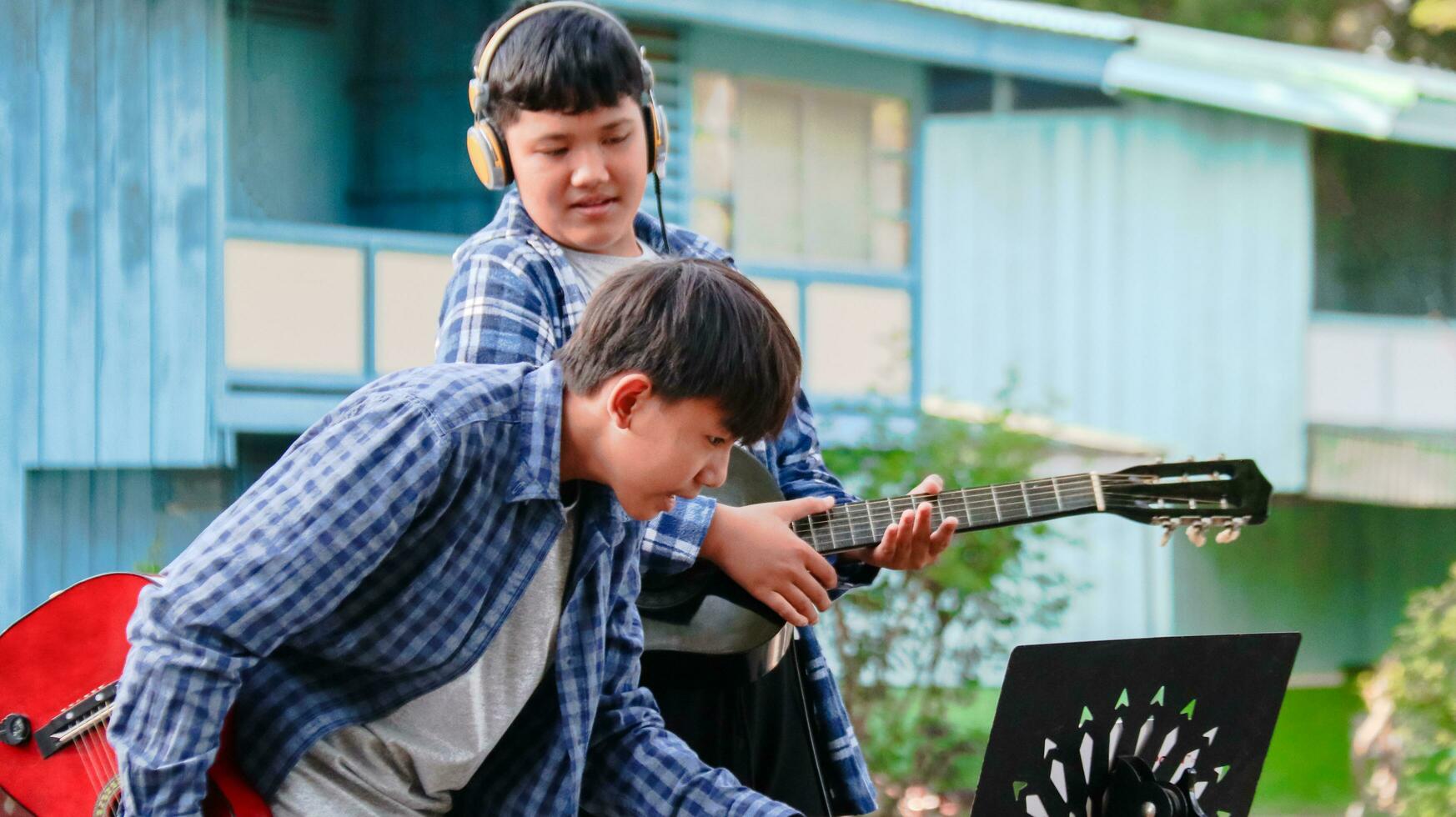 Jeune asiatique garçons sont en jouant acoustique guitares dans de face de une maison concept de apprentissage et gratuit temps Activités photo
