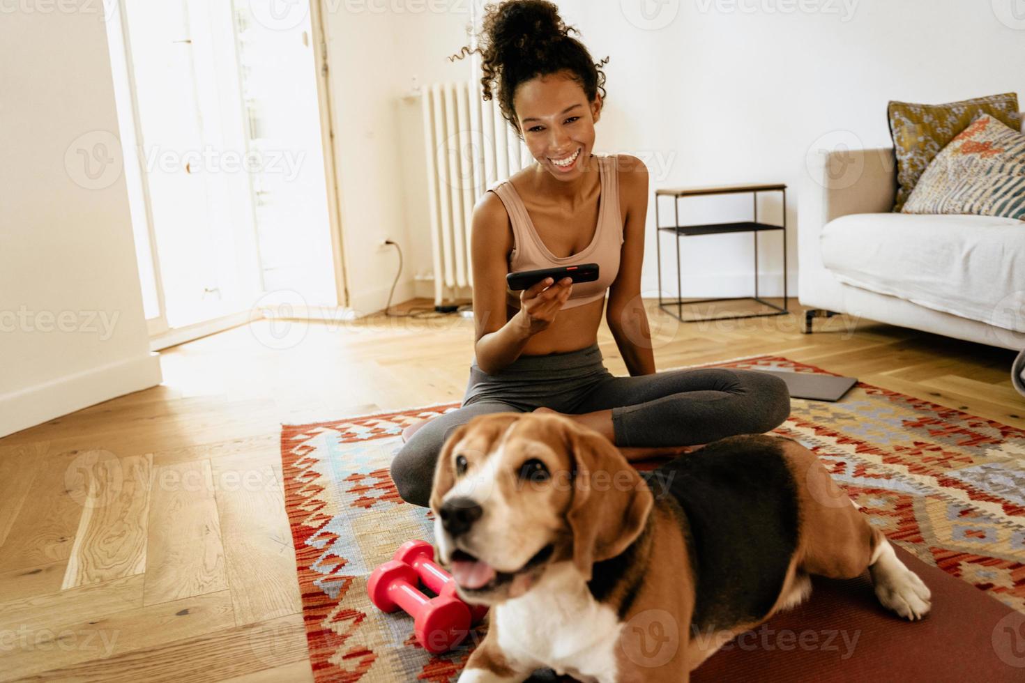 jeune femme noire utilisant un téléphone portable alors qu'elle était assise avec son chien sur un tapis photo