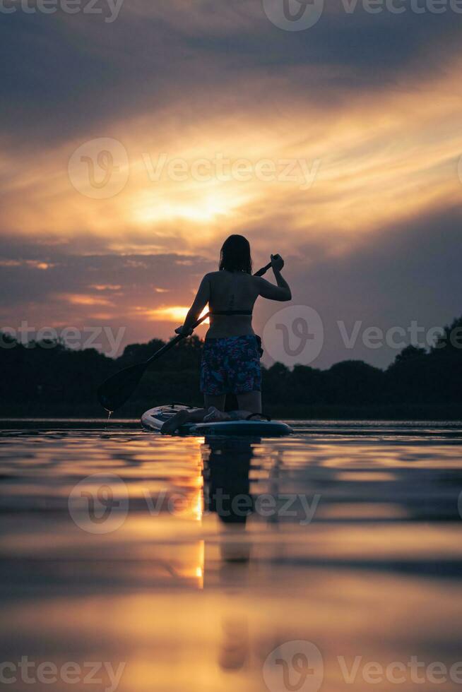 fille sur pagayer planche dans le coucher du soleil photo
